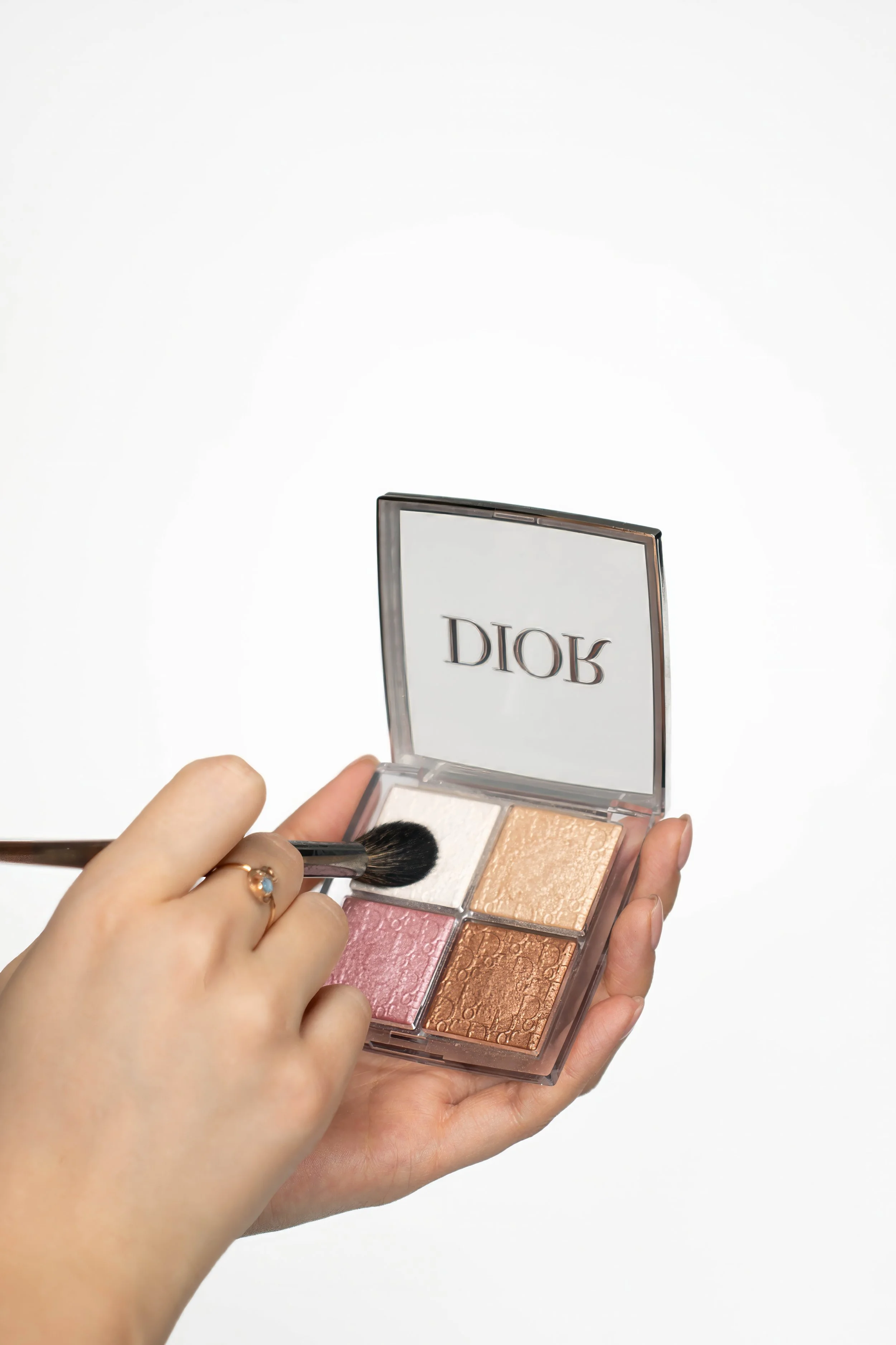 A person holding a Dior eyeshadow palette and applying makeup with a brush.