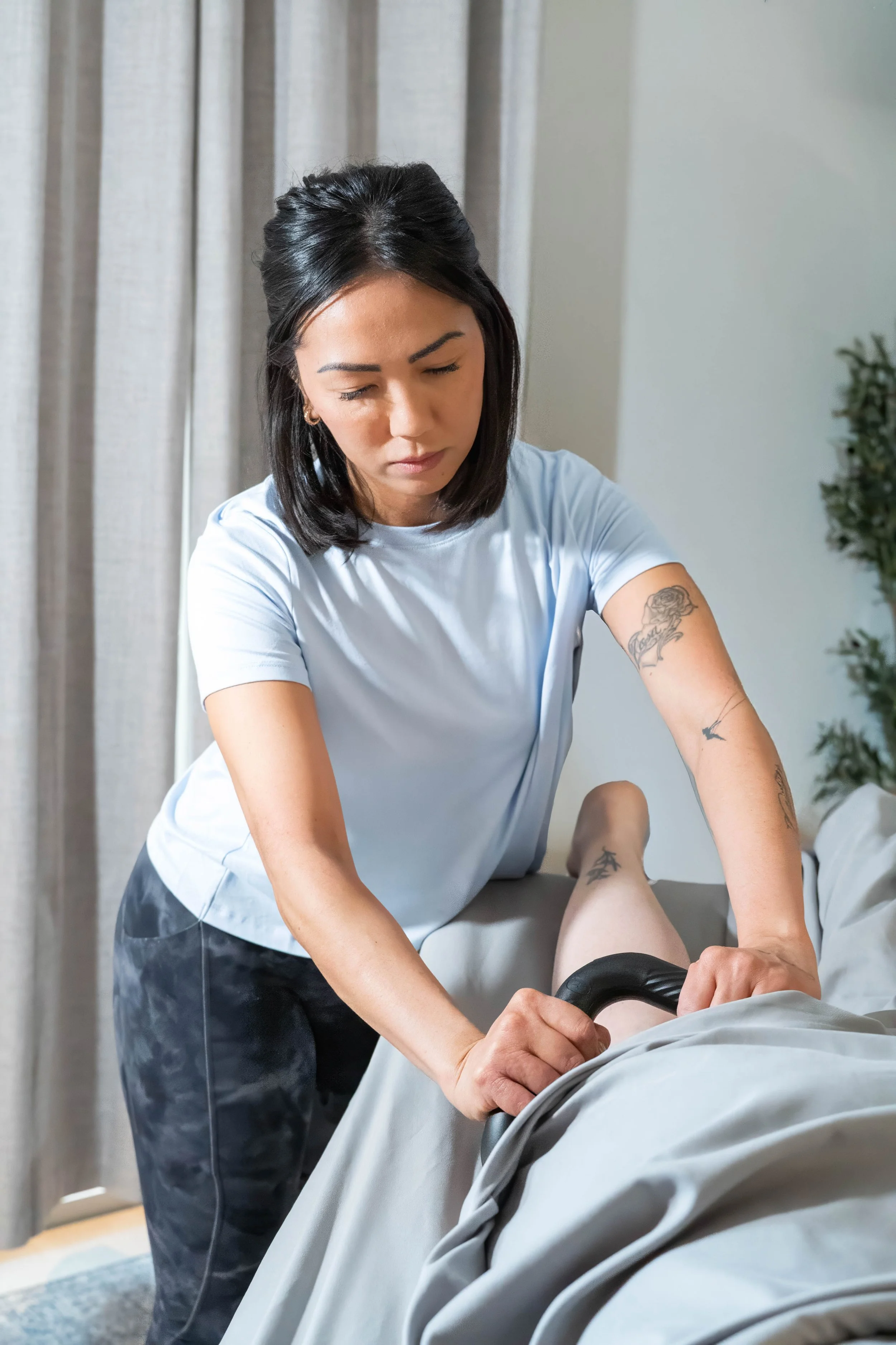 A woman in scrubs providing physical therapy to a patient lying on a bed.