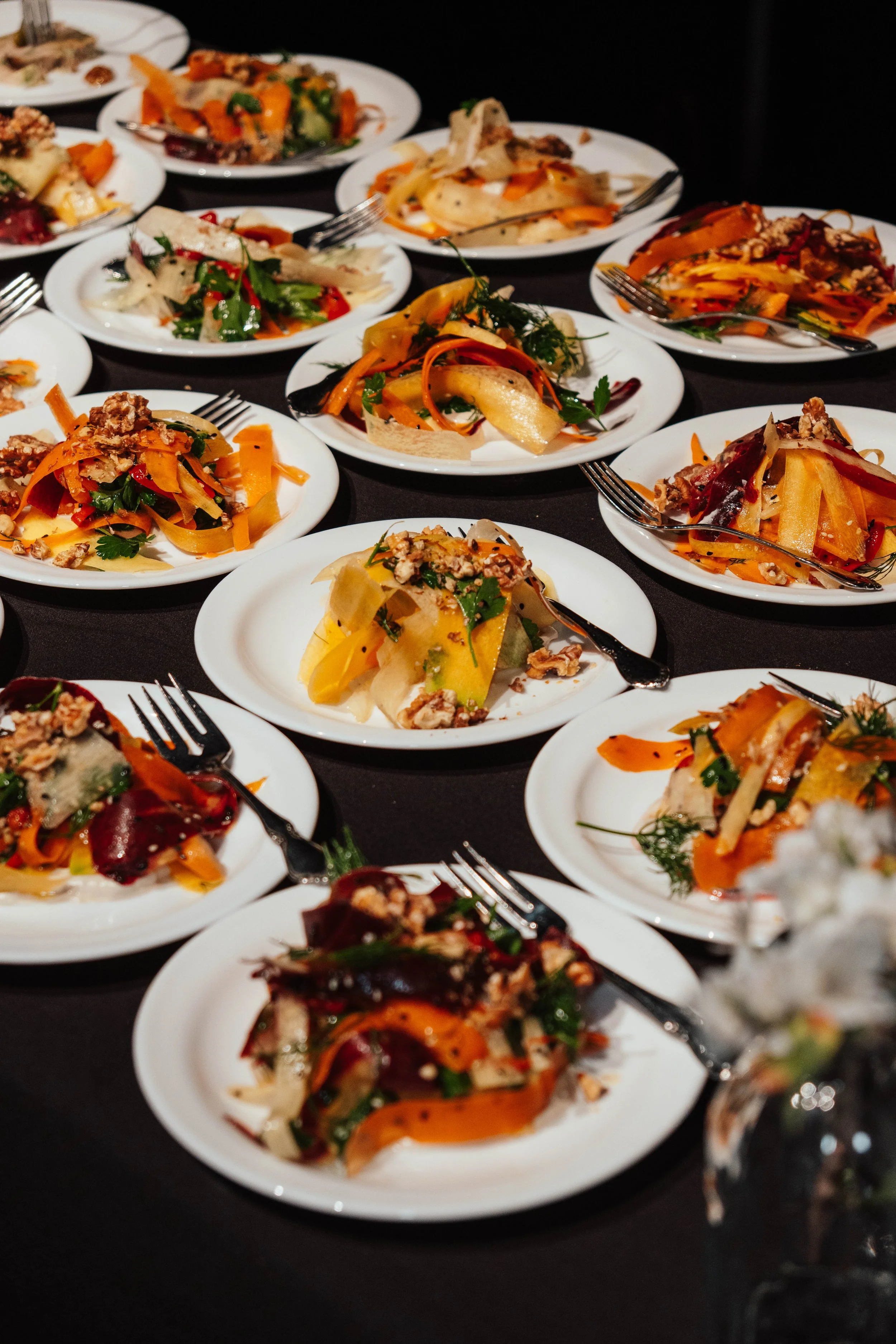 Multiple plates of assorted vegetable dishes with colorful garnishes, arranged on a black table.