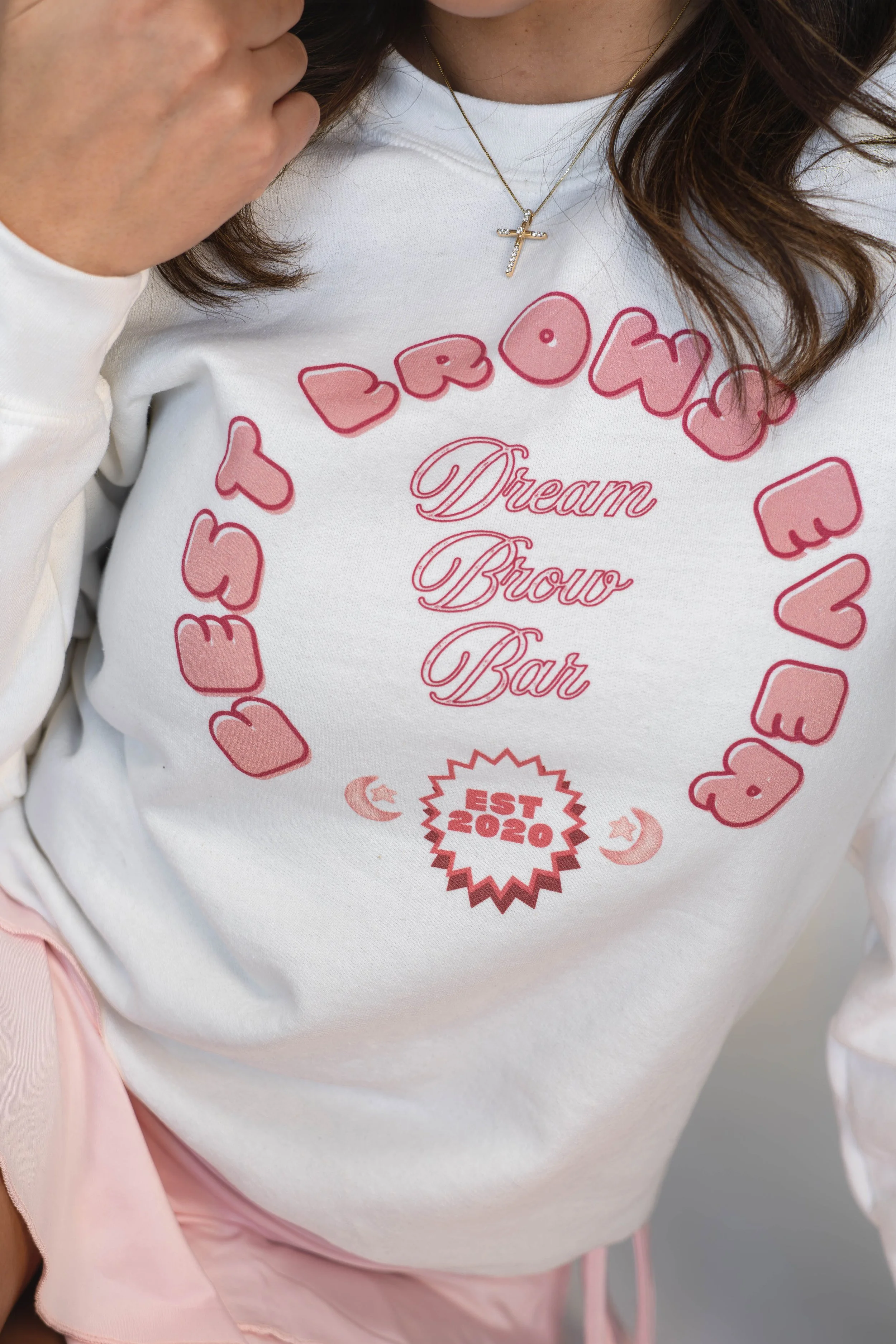 Close-up of a woman wearing a white sweatshirt with pink and red graphics and text that says "Dream, Grow, Bat" inside a heart shape with the brand name "LUSH LOVE" and established date "EST 2020" in the center, along with crescent moon and star symb