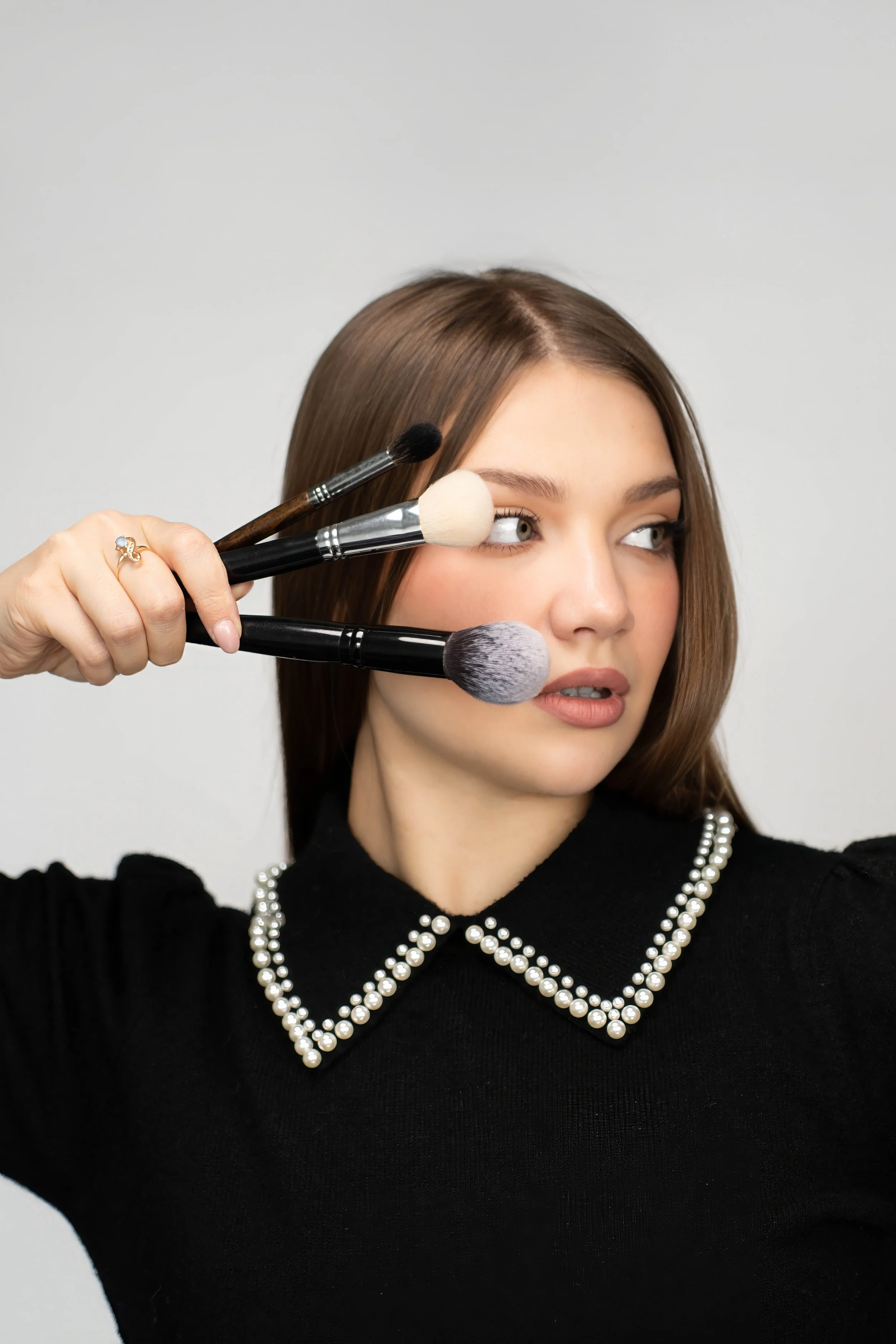 Woman with brown hair holding four makeup brushes near her face.