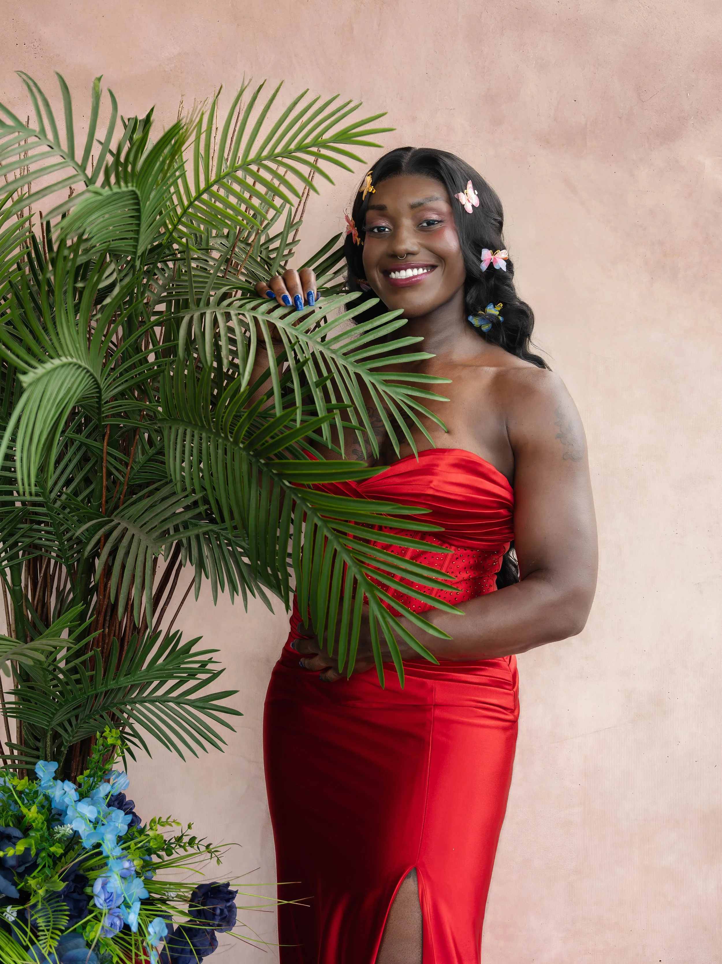 Olympian and bobsleigh athlete Cynthia Appiah smiling in a red gown with butterfly hair accessories, surrounded by tropical greenery during a creative editorial photoshoot in Toronto.