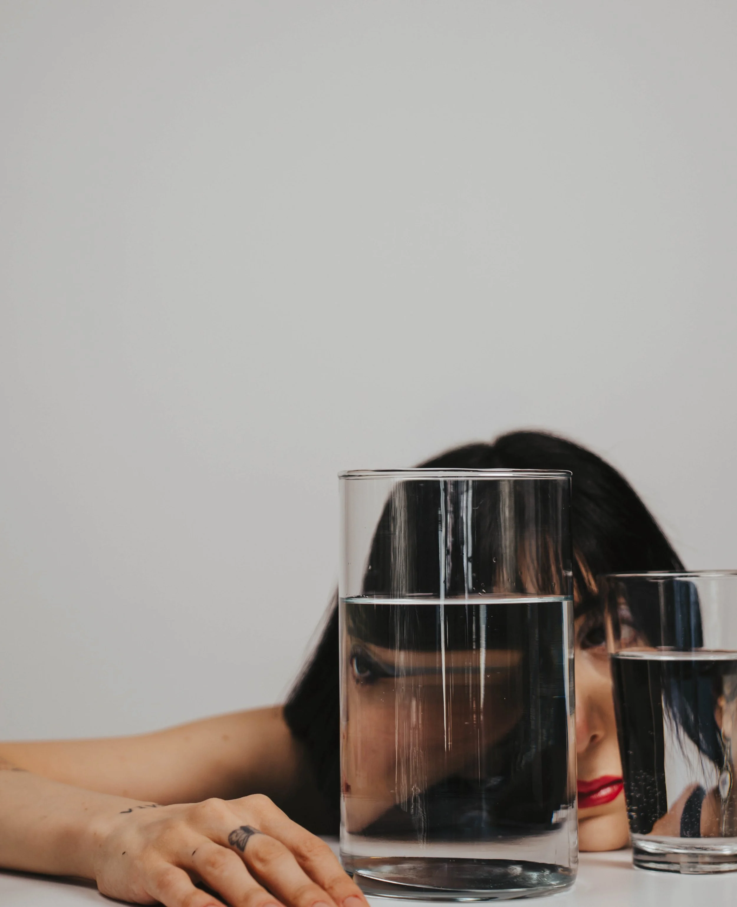 Woman creating surreal self portrait photography using glass and water refraction distortion in a minimalist studio setup with conceptual fine art portrait styling.