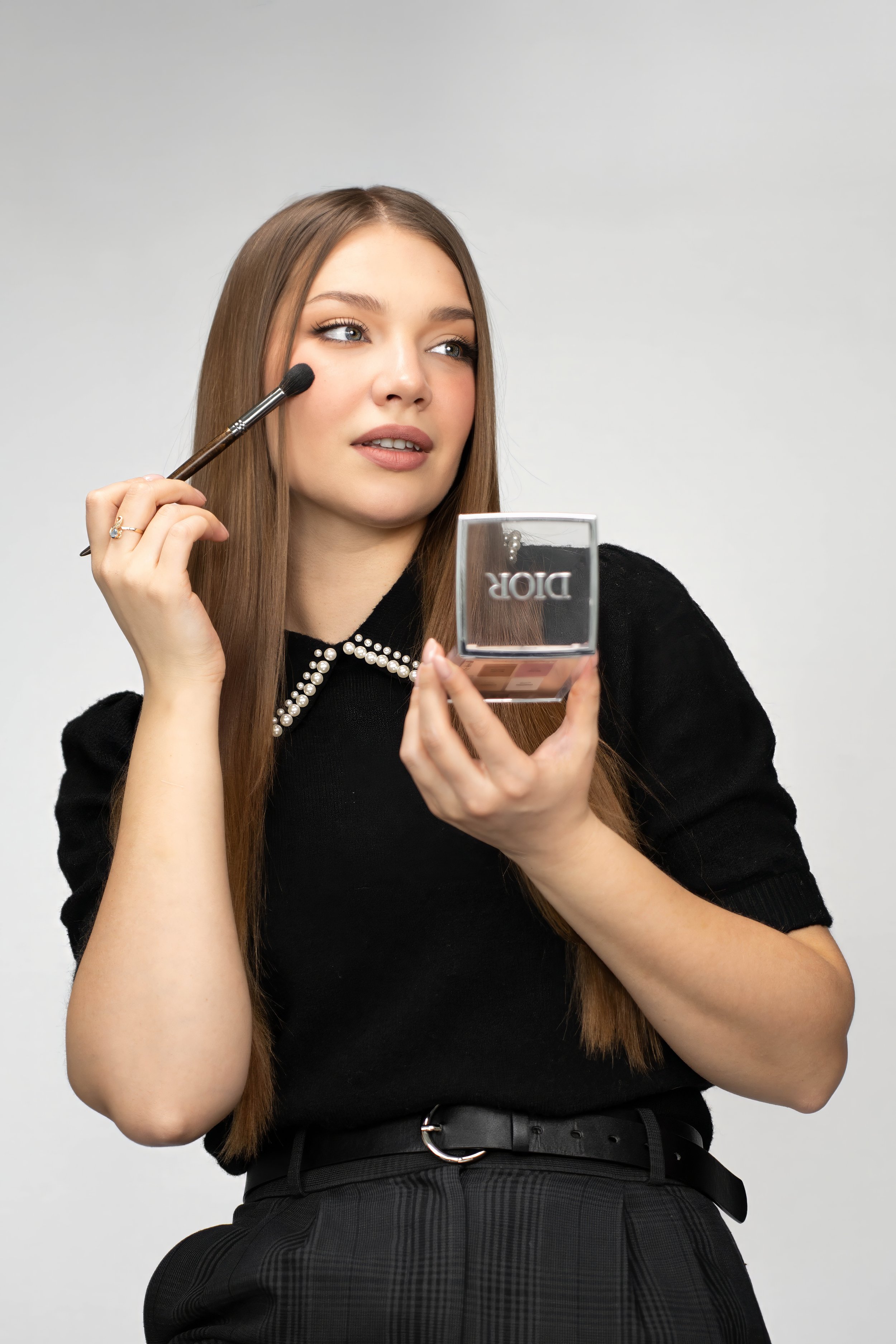 Young woman applying makeup with a brush while holding a Dior makeup compact