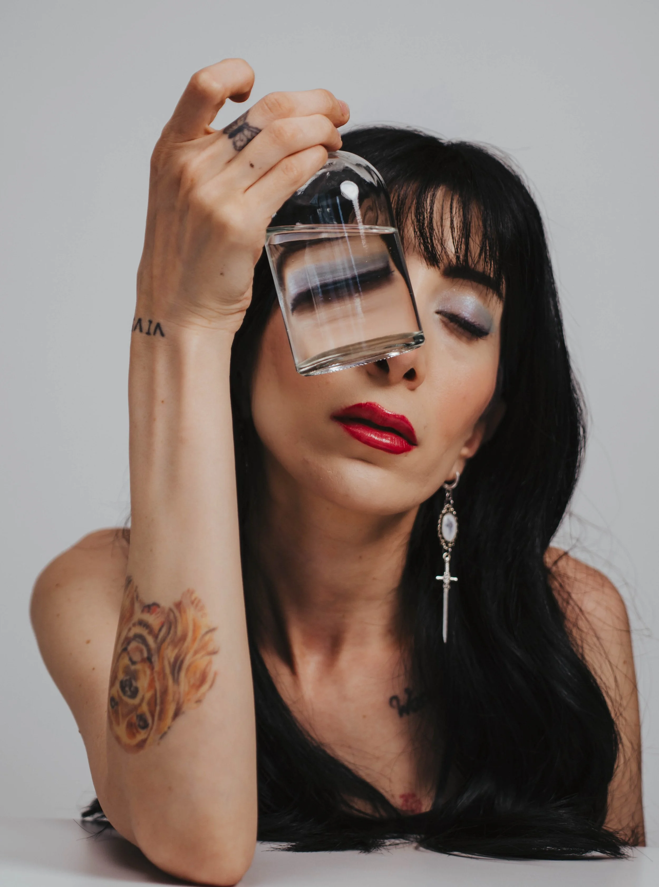 Woman creating surreal self portrait photography using glass and water refraction distortion in a minimalist studio setup with conceptual fine art portrait styling.
