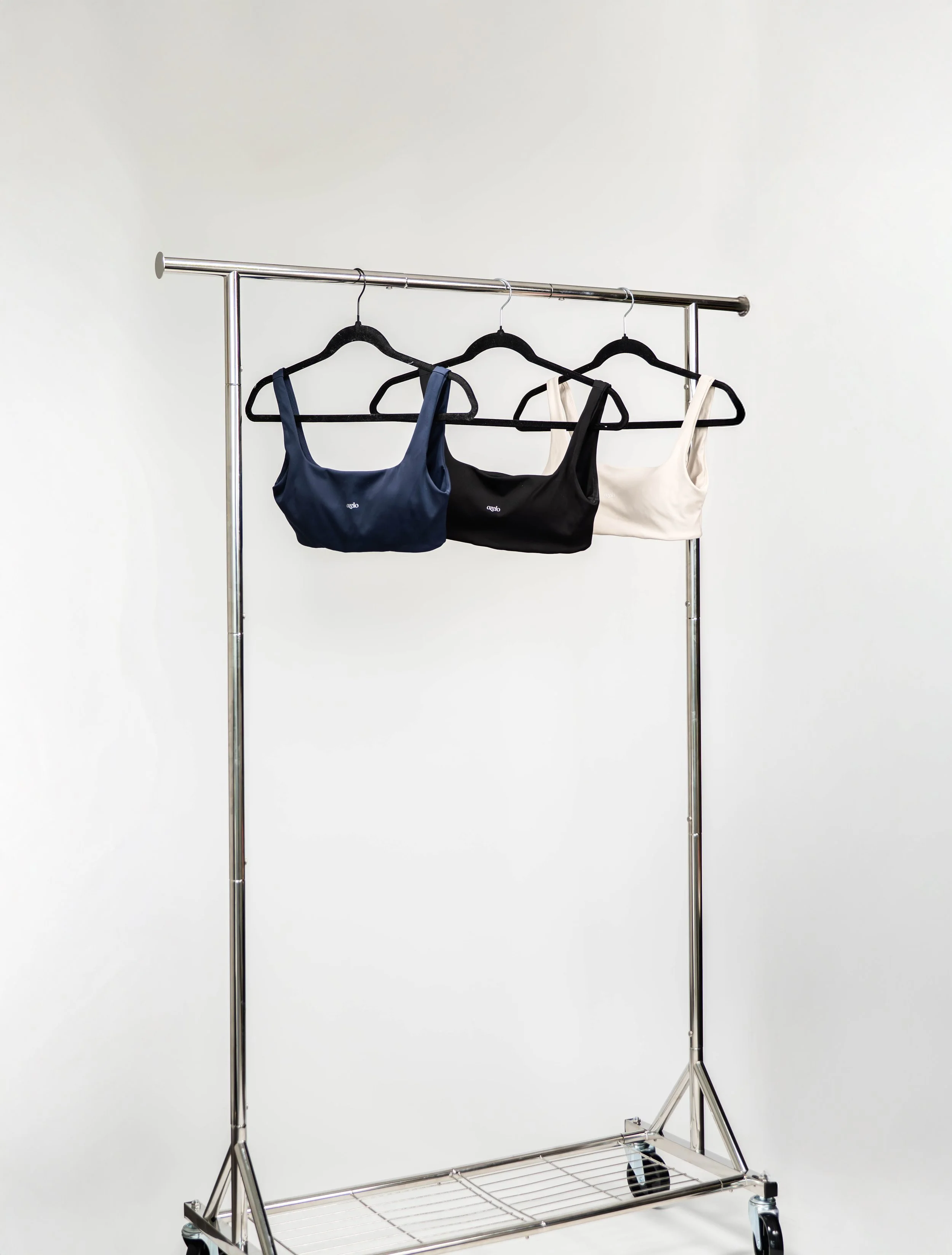Three bras hanging on a metal clothing rack, with one navy blue, one black, and one white, against a plain white background.