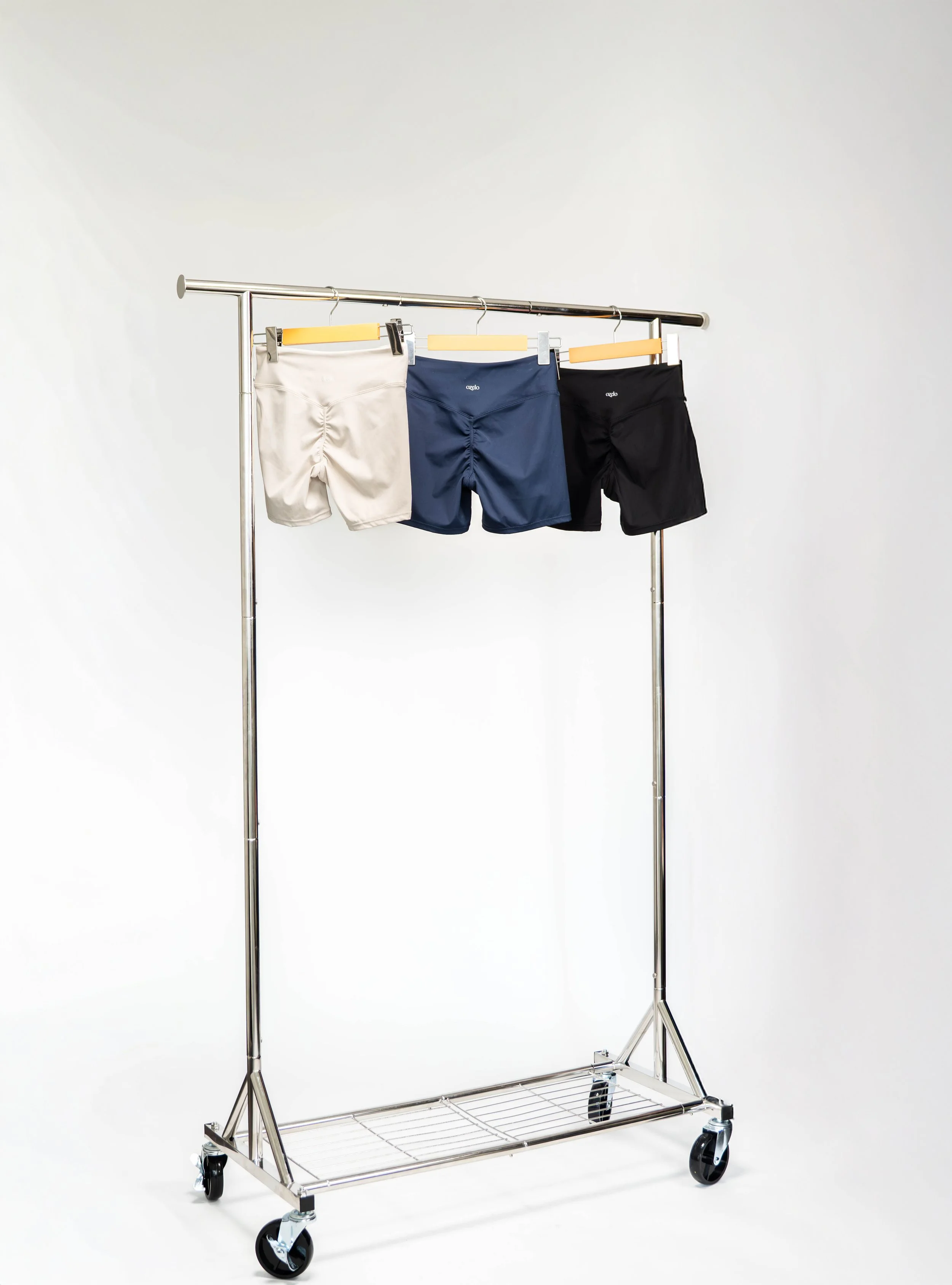 Three pairs of men's boxer briefs in beige, navy, and black hanging on a metal clothing rack with wheels against a plain white background.