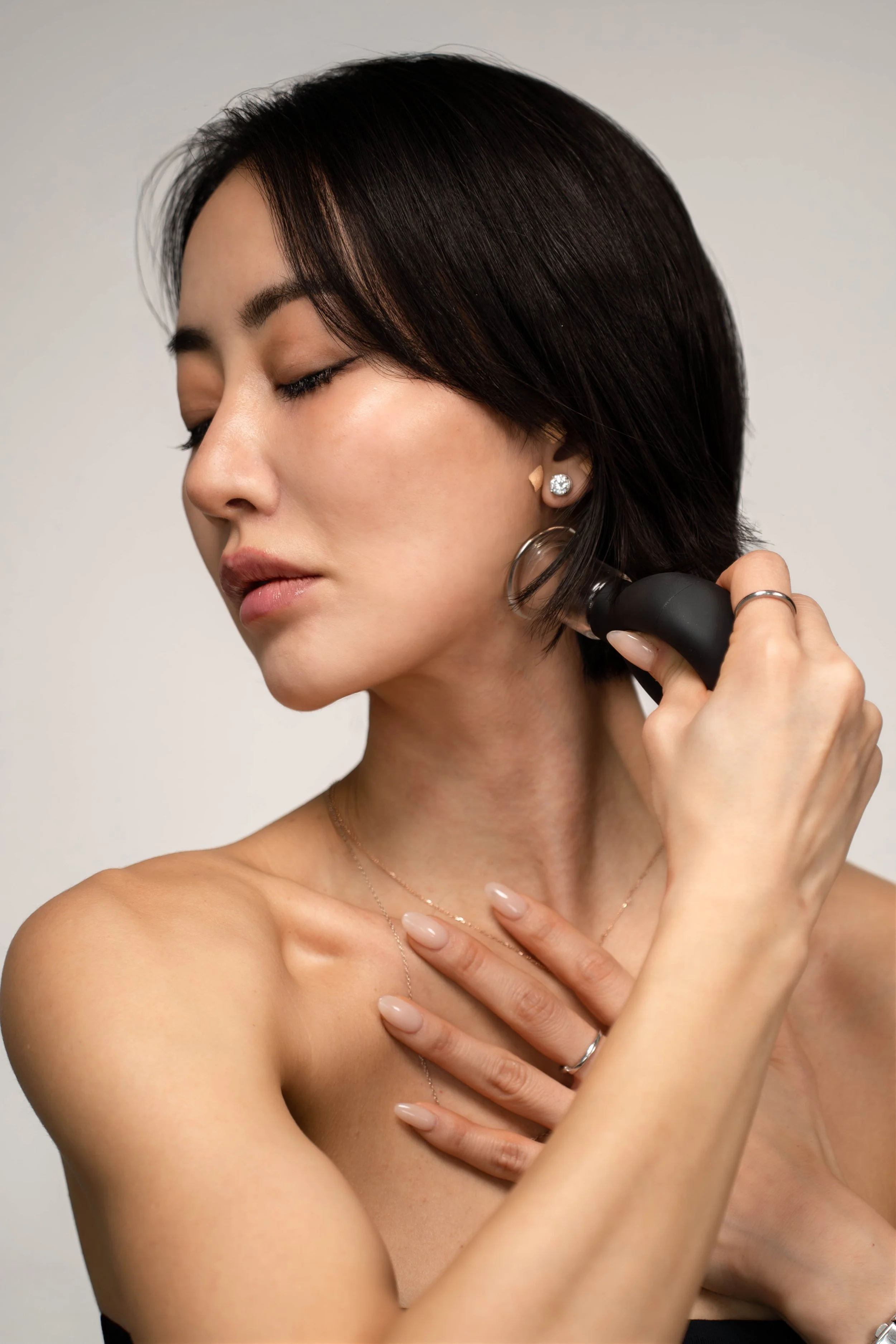 A woman with short dark hair using an electronic facial cleansing device on her face, with her eyes closed and a serene expression.