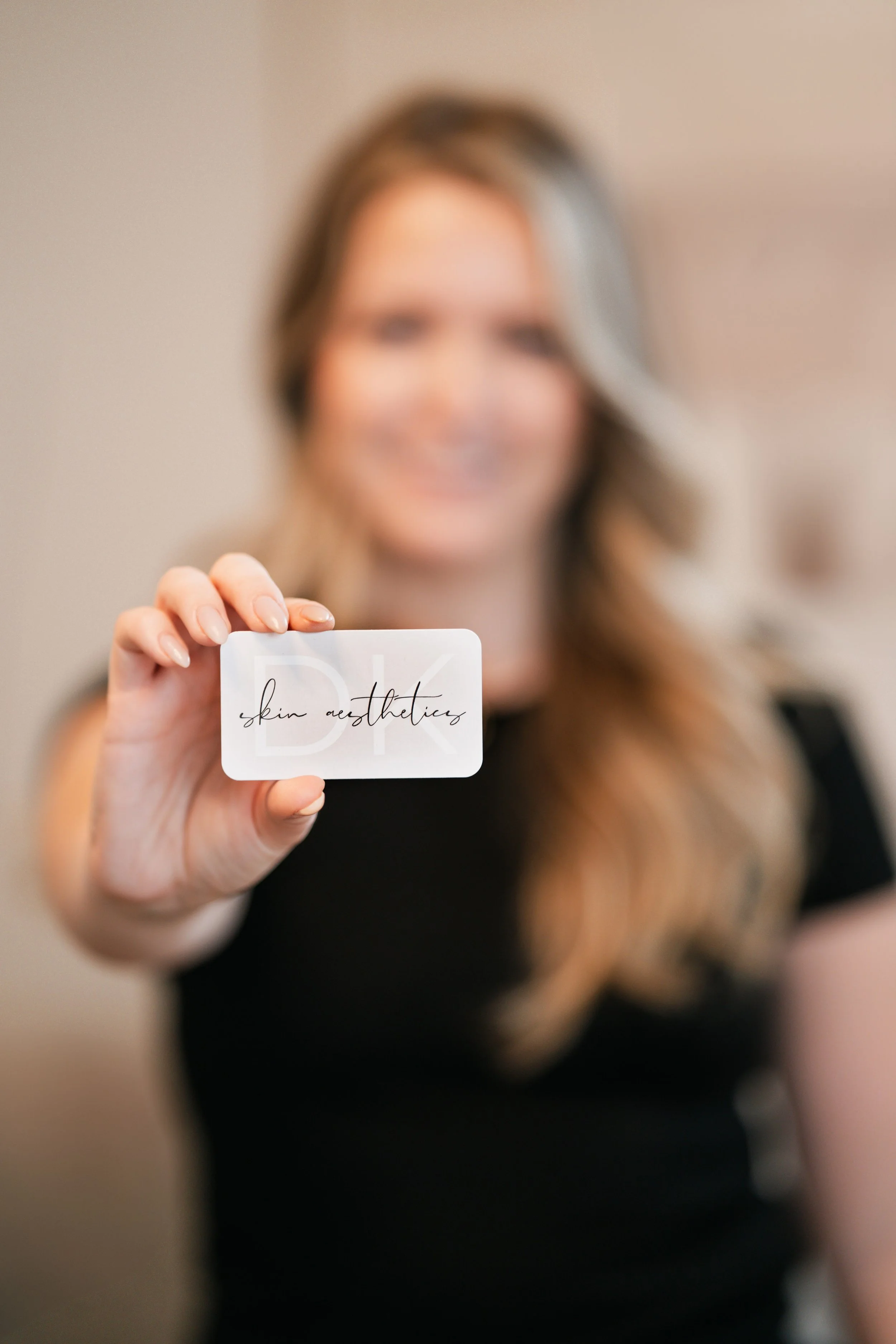 Professional branding photo of a beauty business owner holding a skincare aesthetics business card with soft luxury studio lighting.