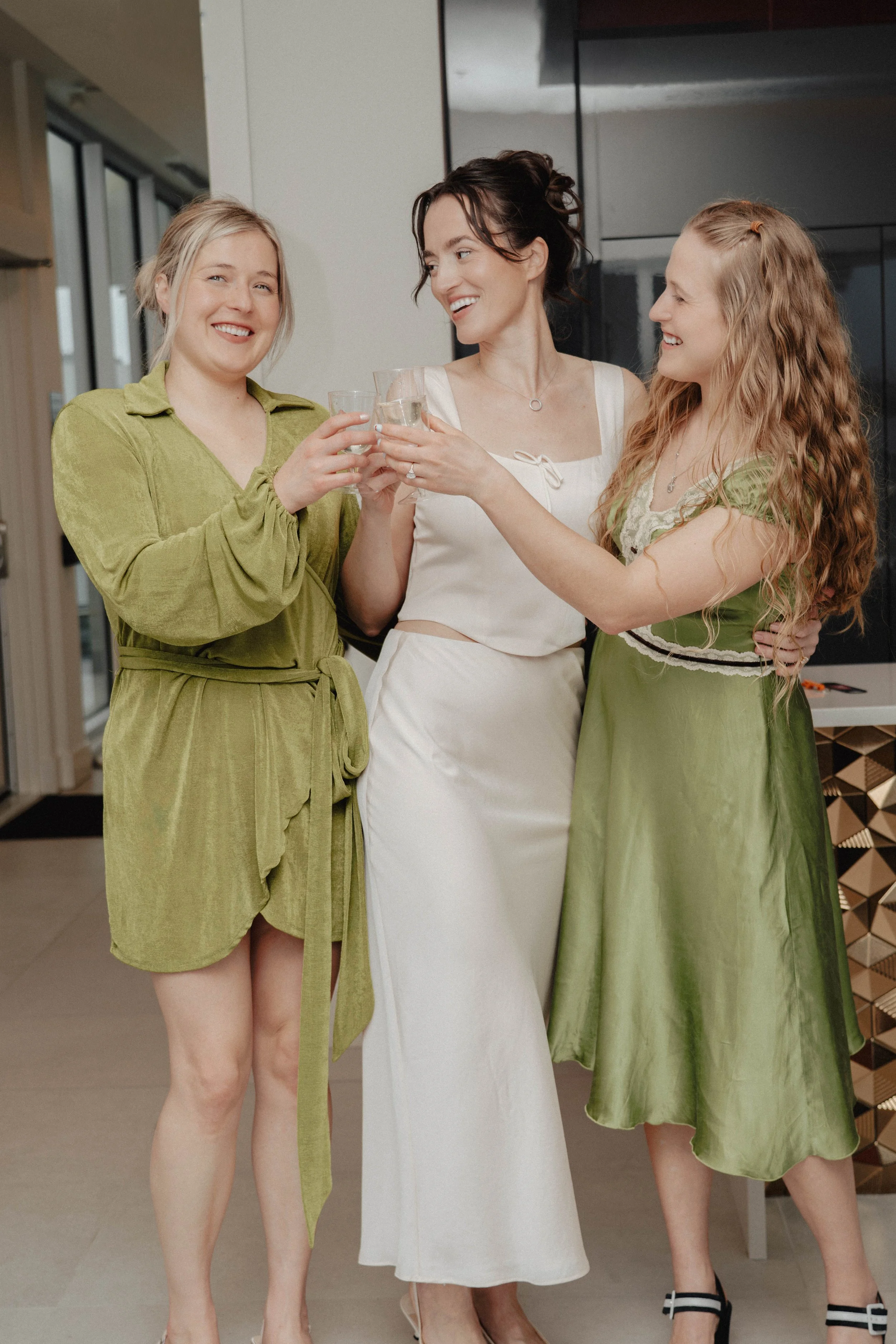 Three women at a social gathering, holding glasses and smiling.