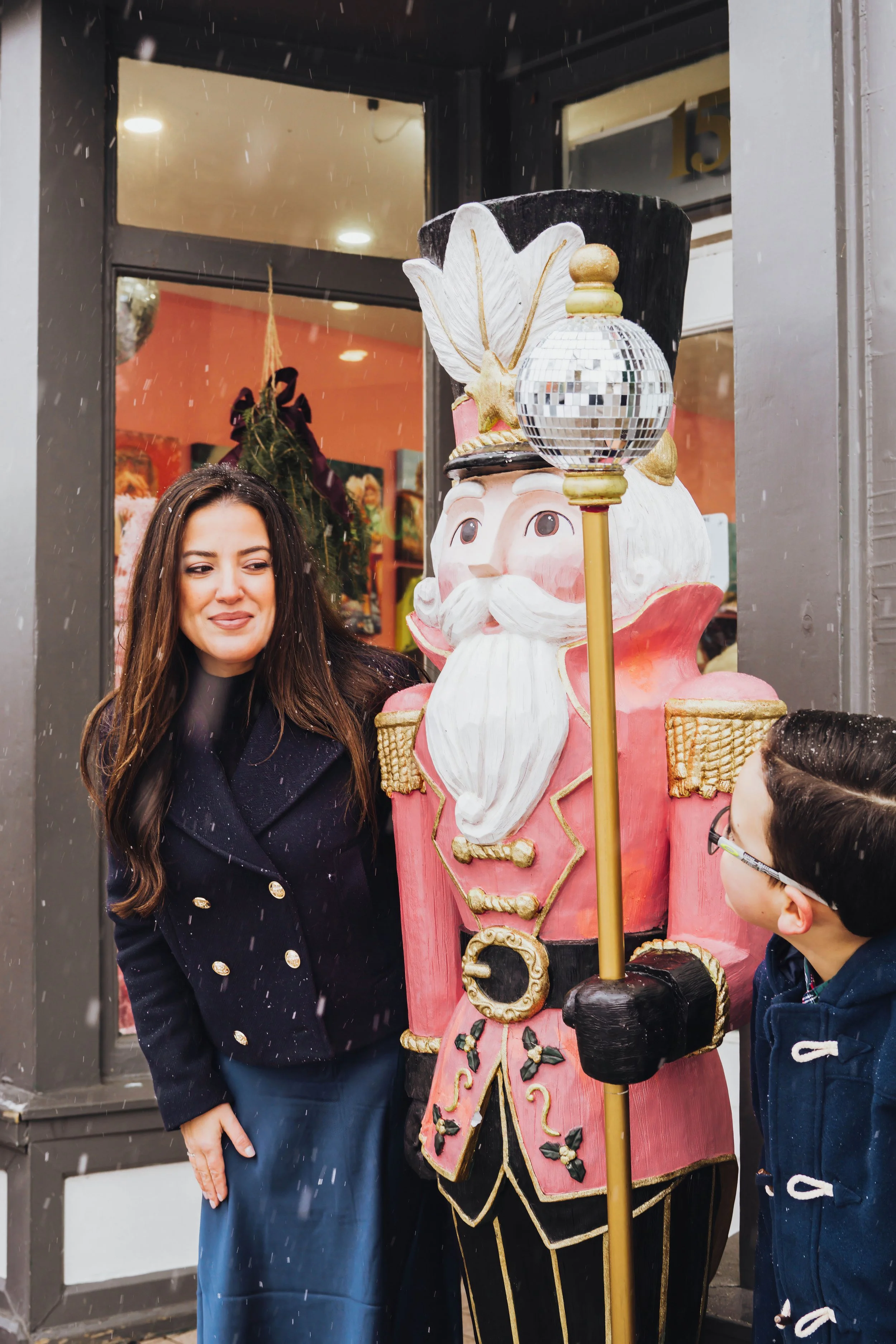 Christmas family photography in Niagara-on-the-Lake featuring a mother and child beside a festive pink nutcracker during a snowy holiday photo session.