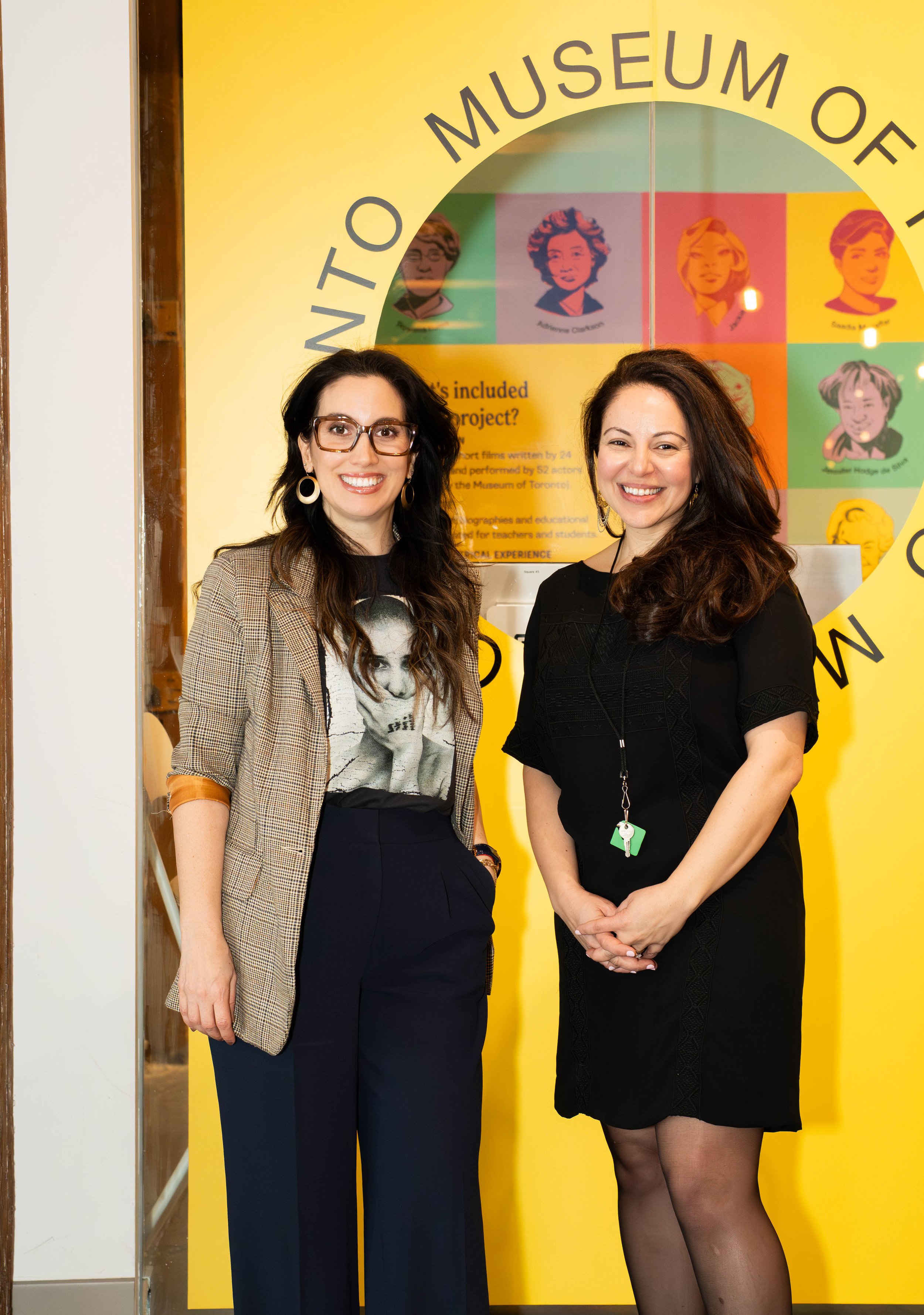 Two women standing and smiling in front of a colorful display at the Toronto Museum of Education.