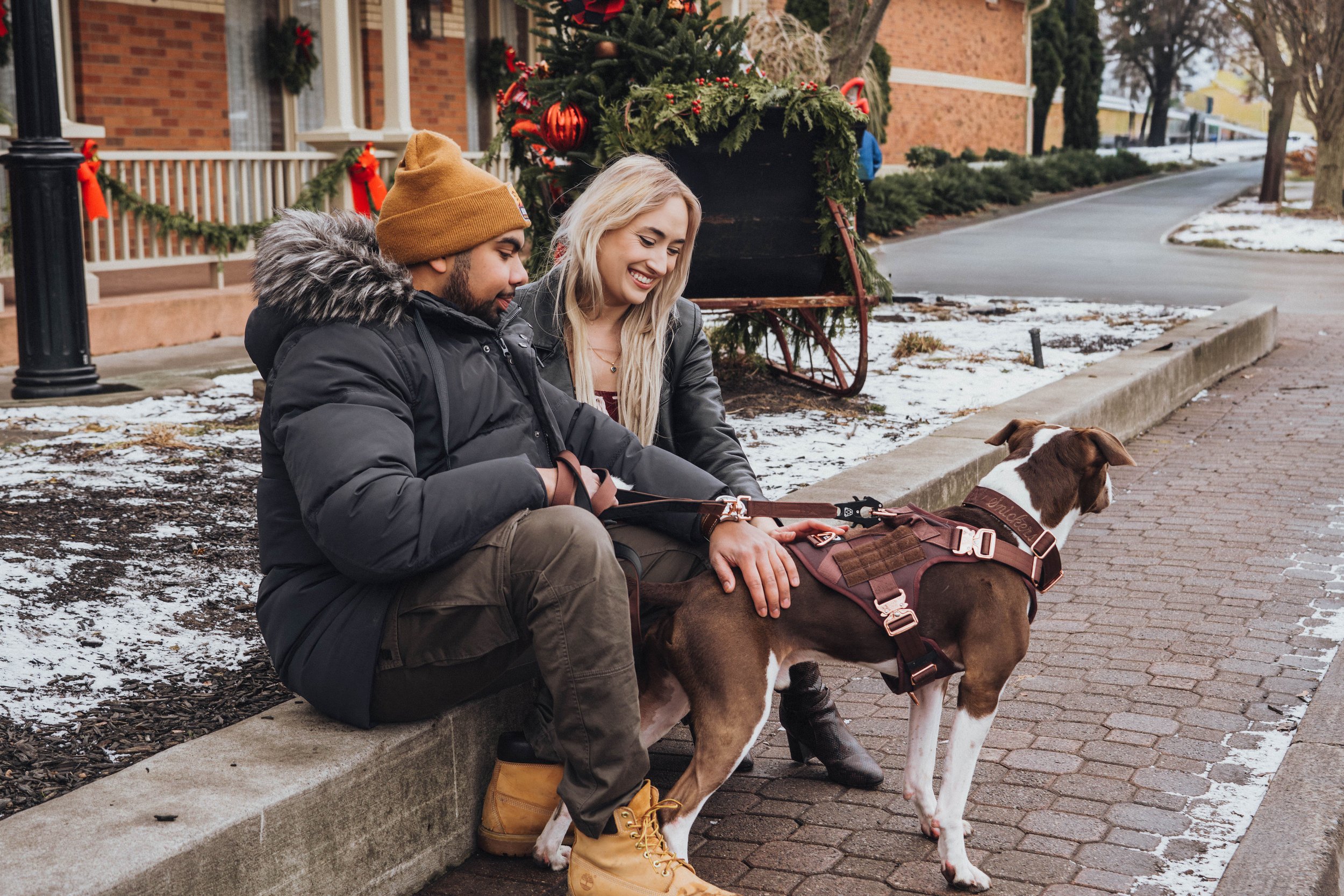 Christmas couple photography in Niagara-on-the-Lake featuring a couple with their dog surrounded by festive holiday decorations and a snowy Christmas setting.