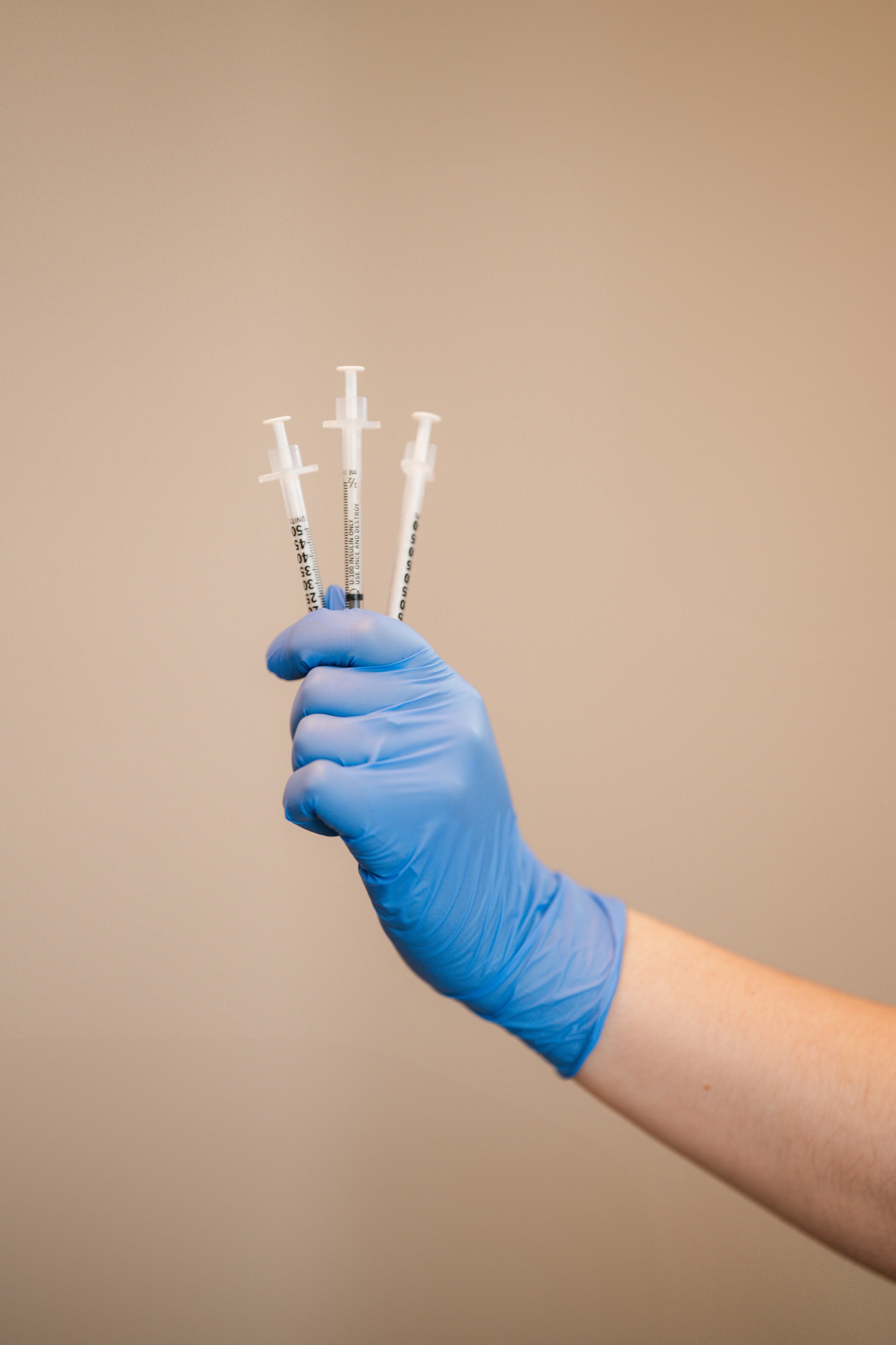 Close-up branding photo of gloved hands holding skincare syringes in a clean luxury wellness studio.