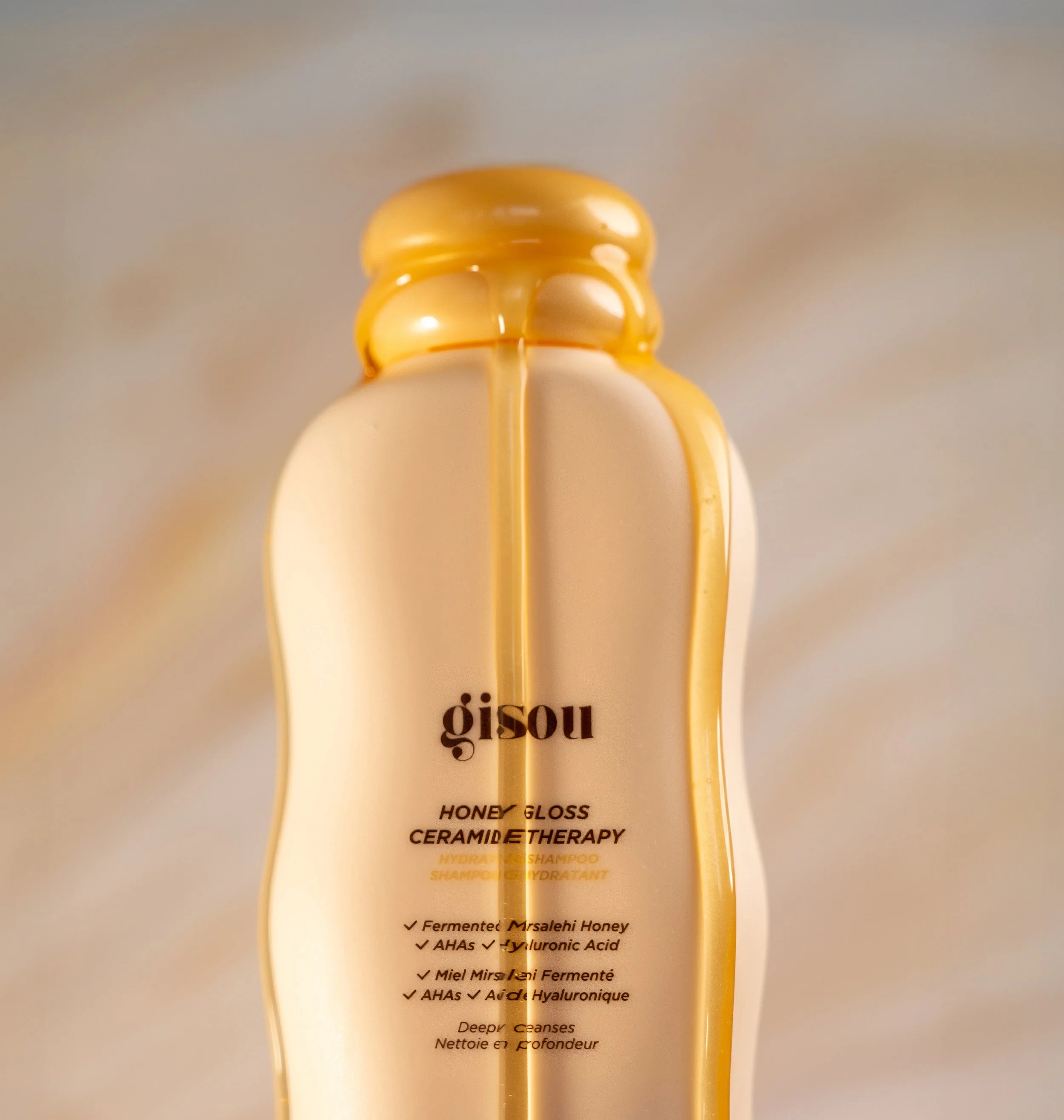 A bottle of Gisou Honey Gloss Ceramide Therapy hydrating shampoo with honey drizzled over the top.