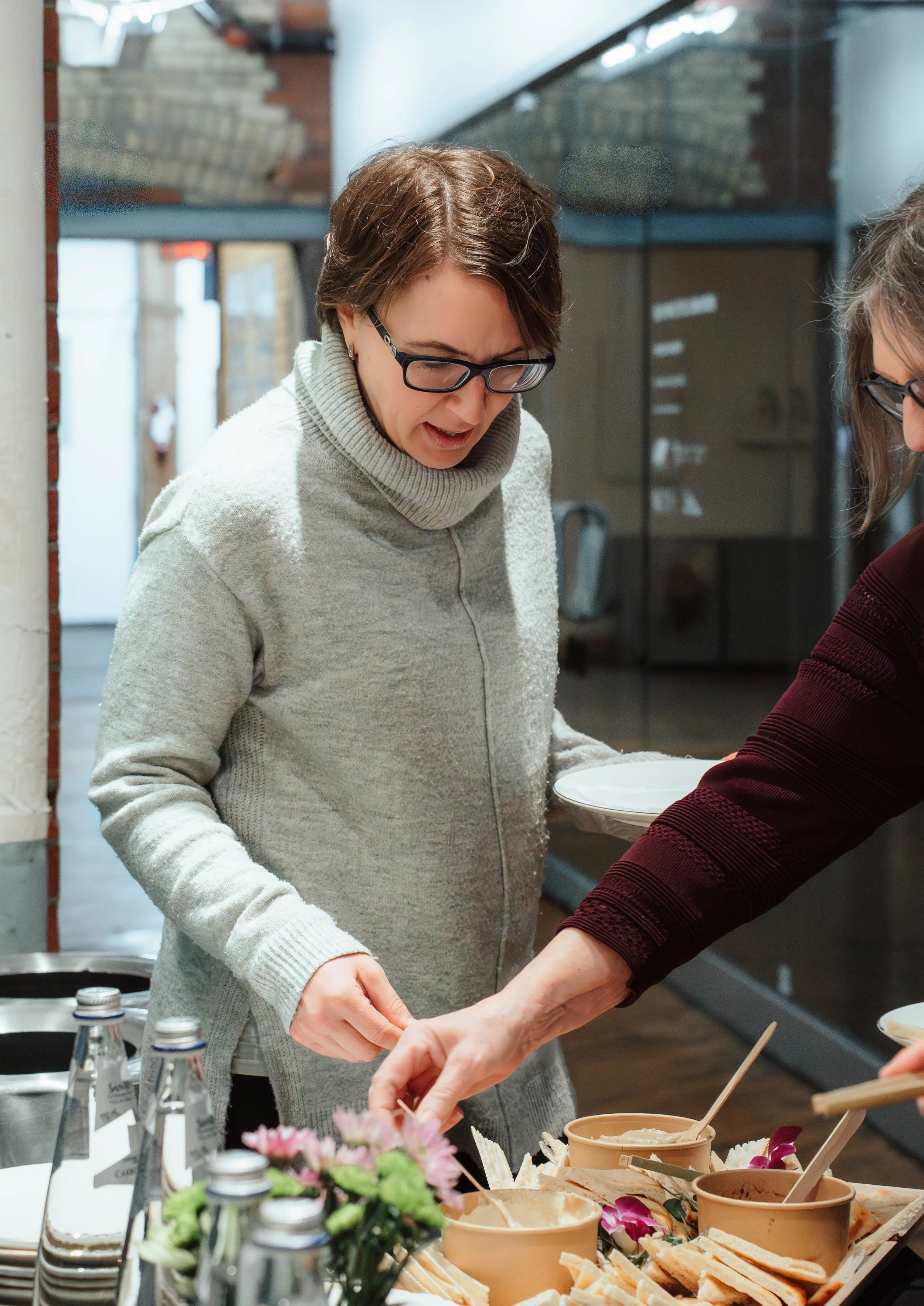 Women serving ice cream at a dessert bar with various toppings and bottled water