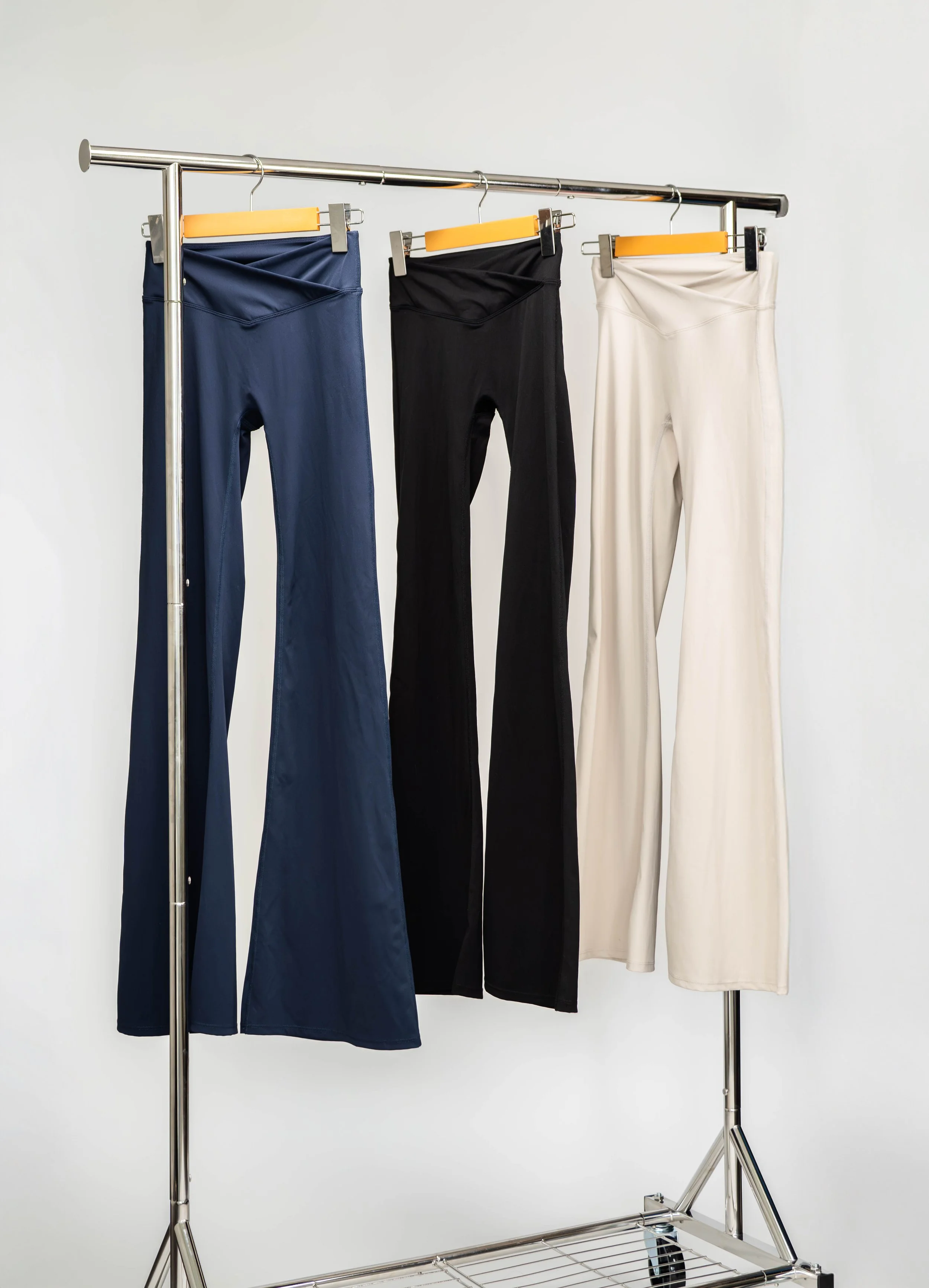 Three pairs of pants in navy, black, and white hanging on a clothing rack.