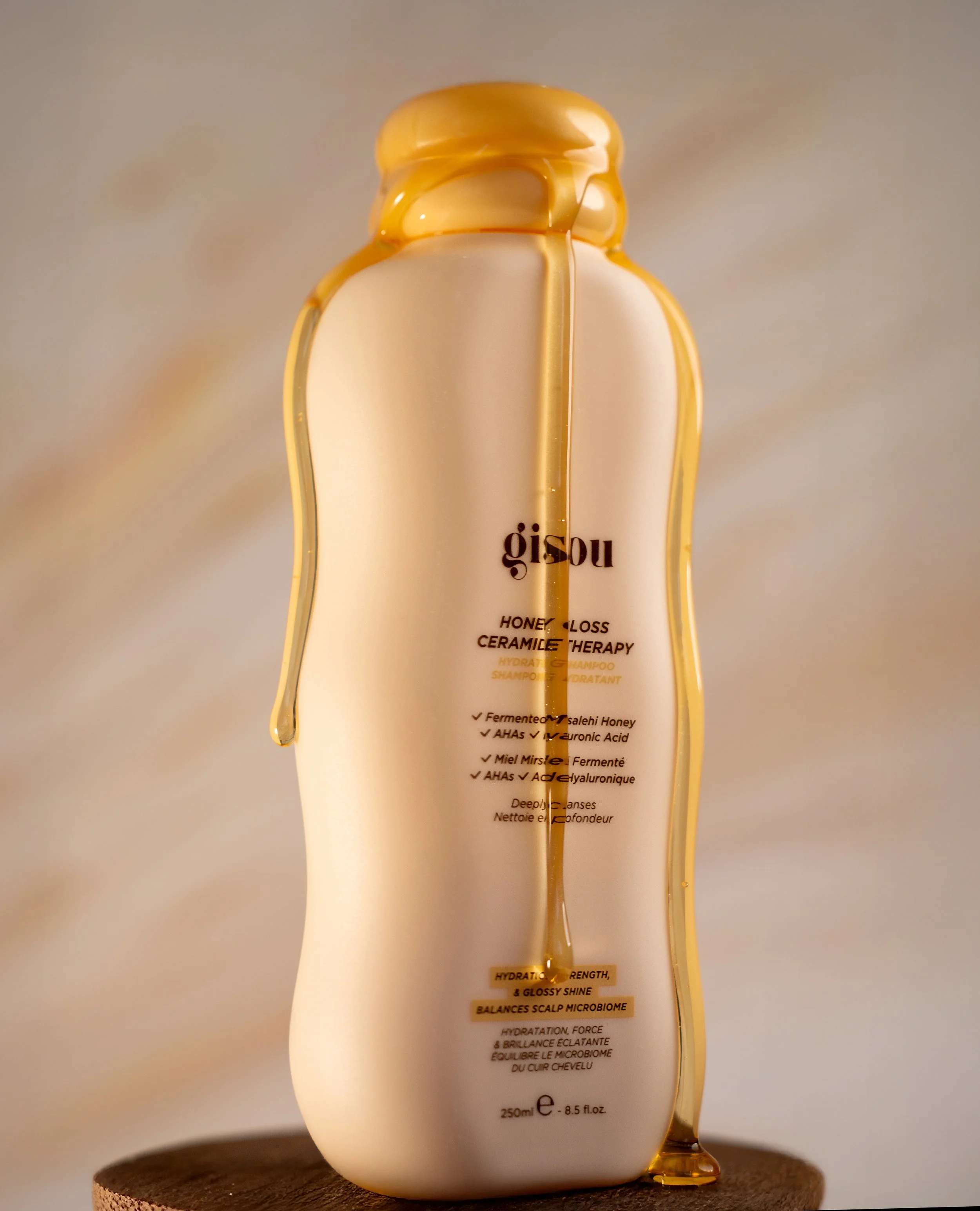Gisou Honey Gloss Ceramide Therapy shampoo bottle with honey dripping down the sides, placed on a wooden surface.