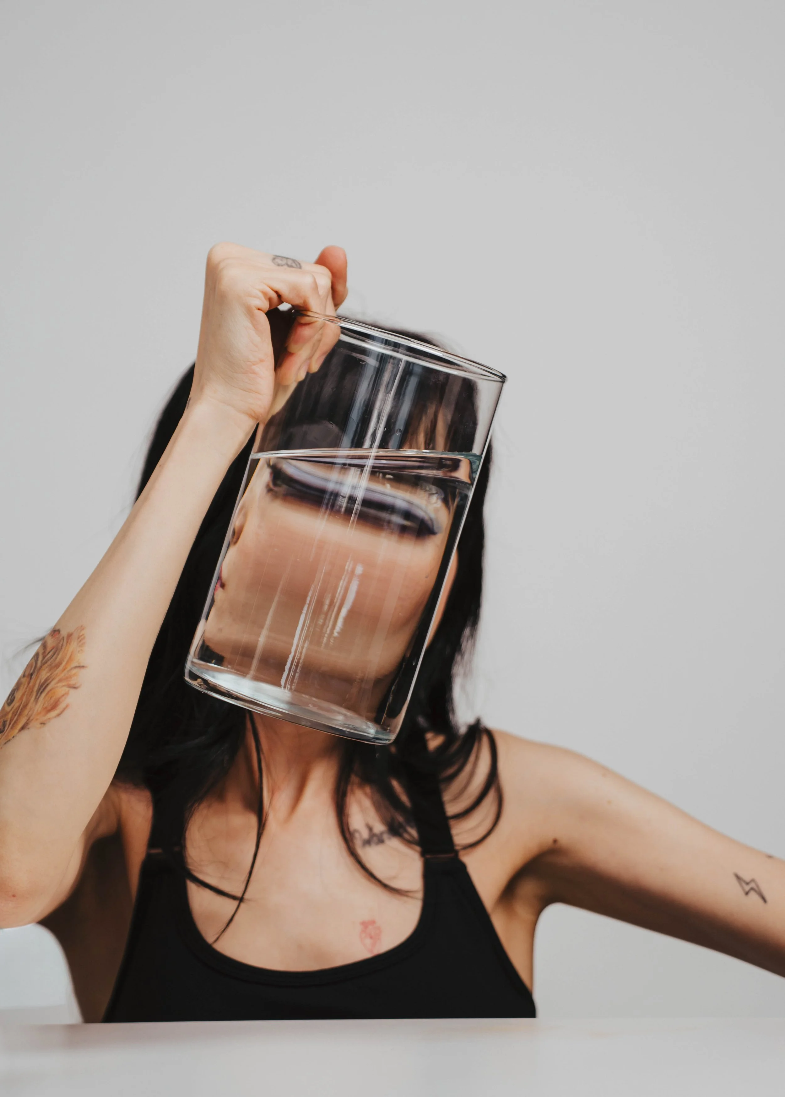 Woman creating surreal self portrait photography using glass and water refraction distortion in a minimalist studio setup with conceptual fine art portrait styling.