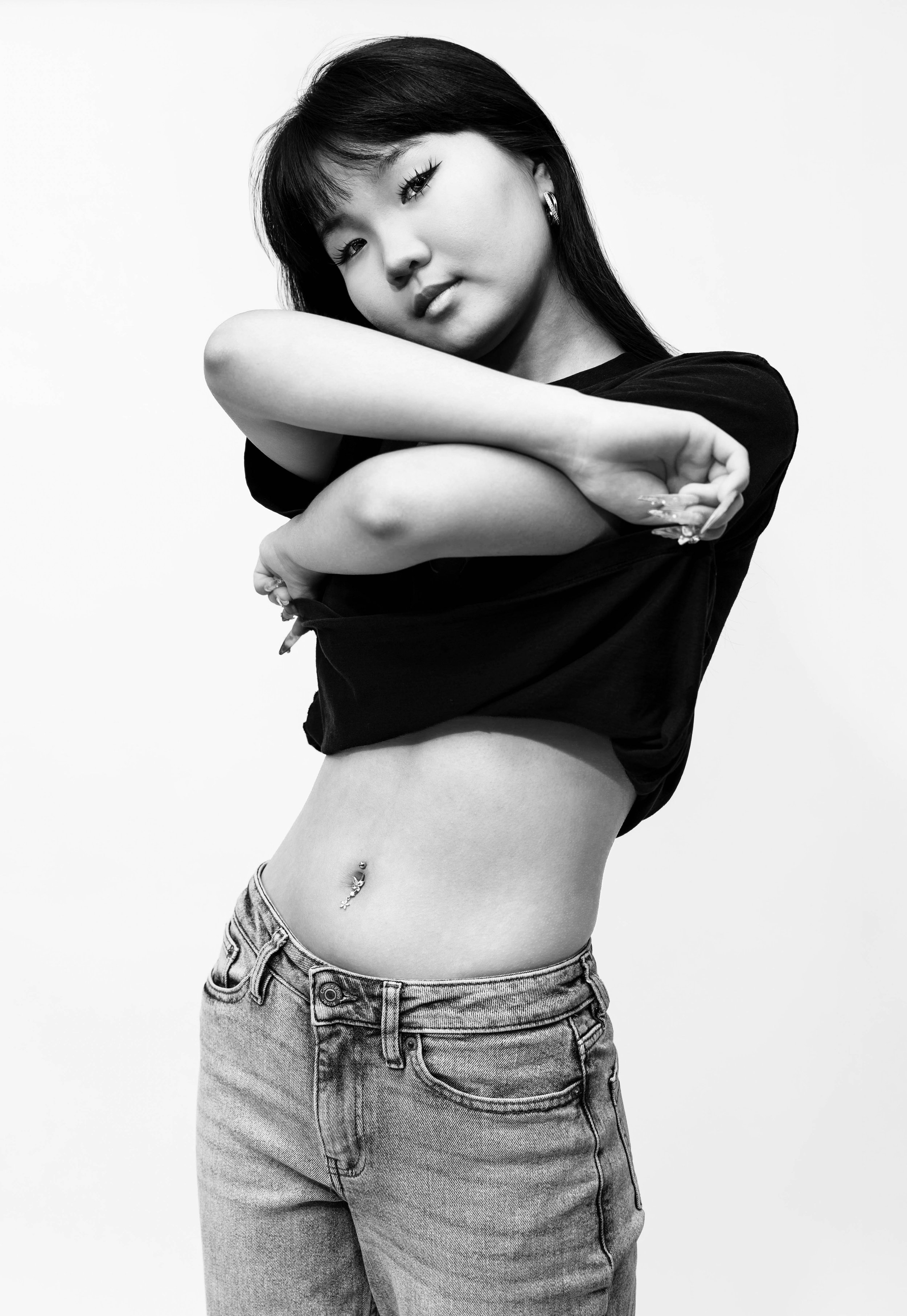 Black and white editorial studio portrait of Dana wearing a black cropped T-shirt and jeans, posing with her arms crossed in front of her against a white backdrop, photographed by Lara Grace Creative Studio in Toronto.