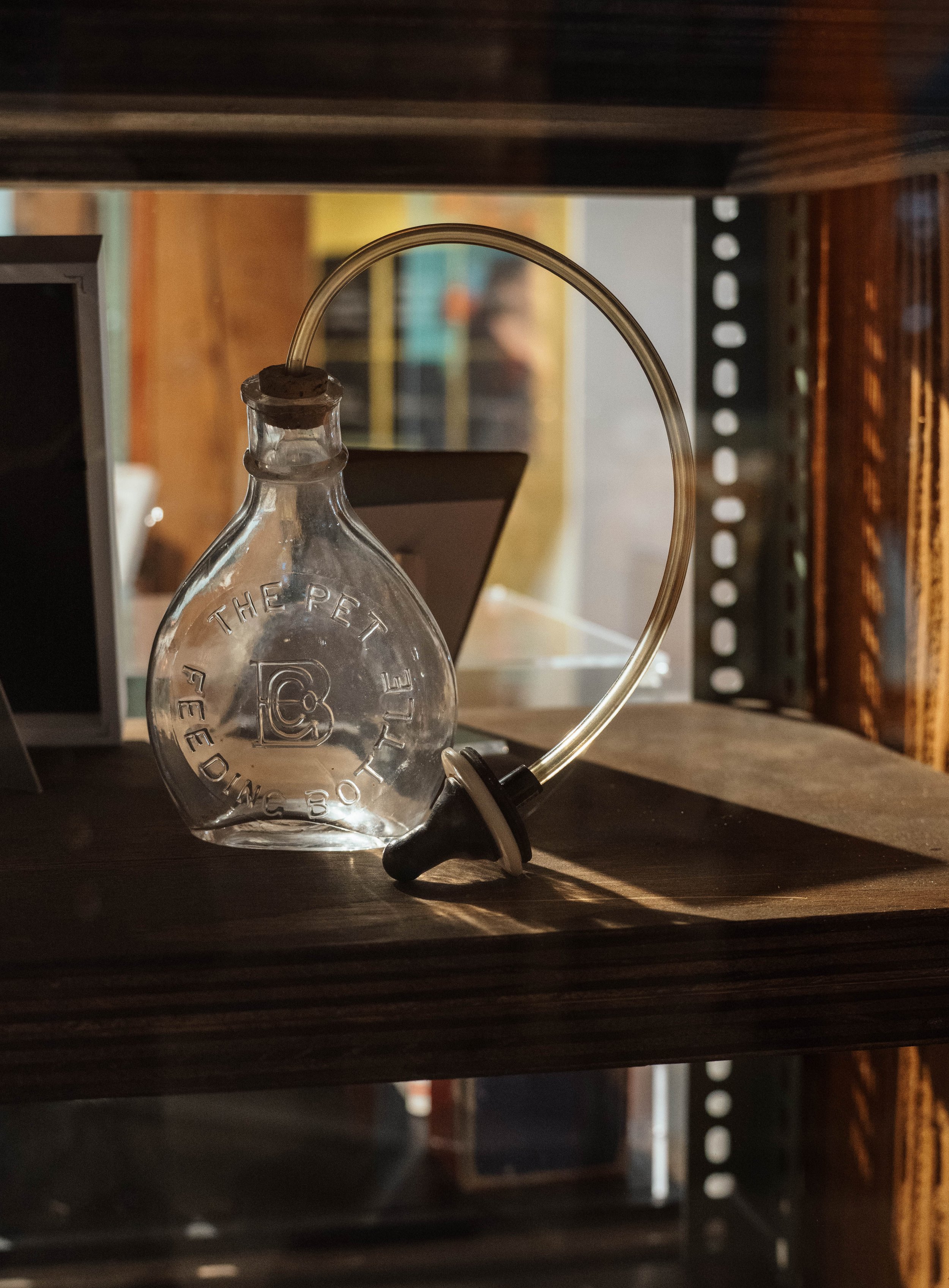 A glass perfume bottle with a black and white cap, and a curved clear tube attached to it, placed on a wooden surface in a dimly lit room.