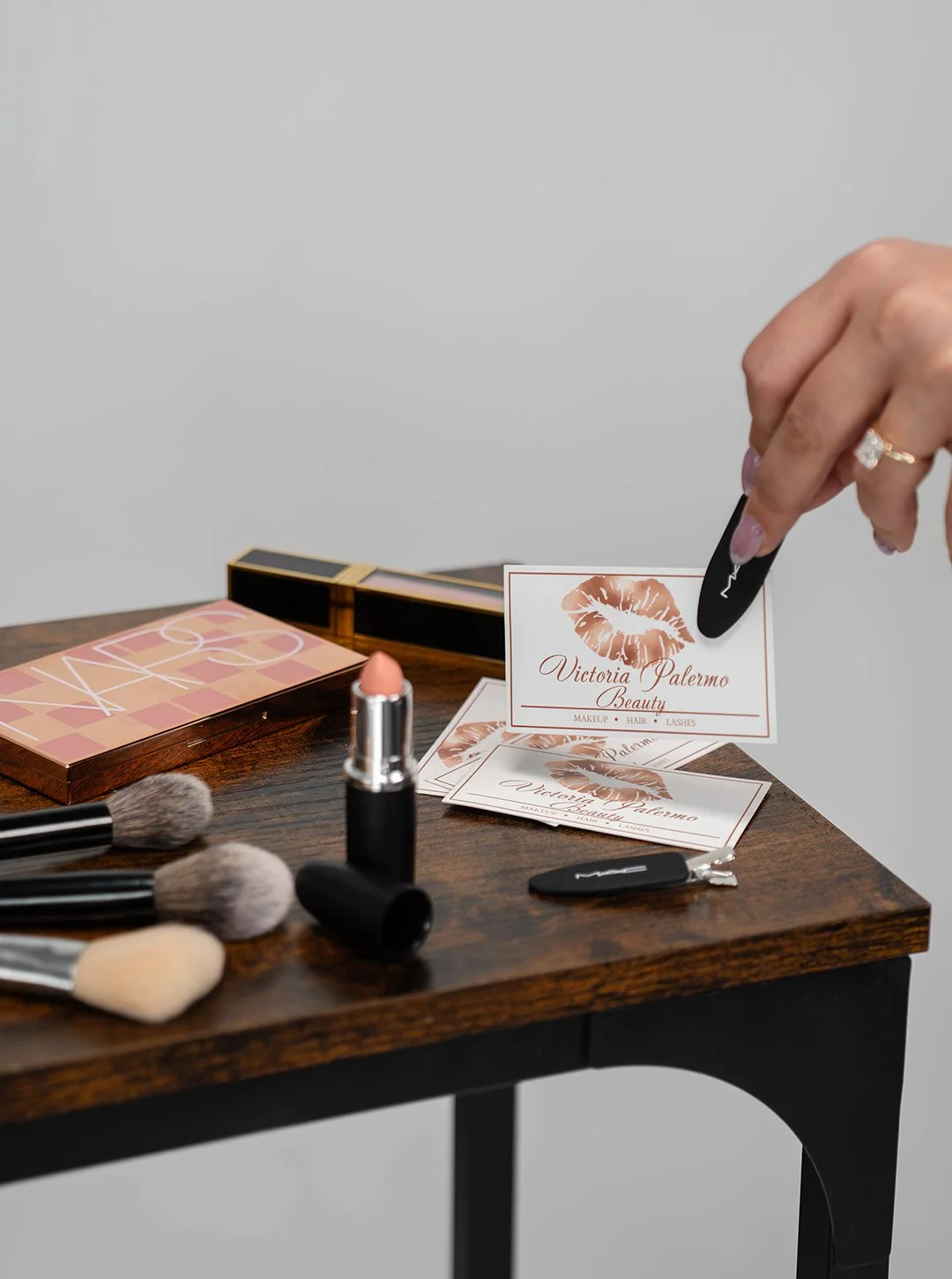Makeup and beauty products on a wooden table, including brushes, lipstick, and business cards for Victoria Palermo Beauty.