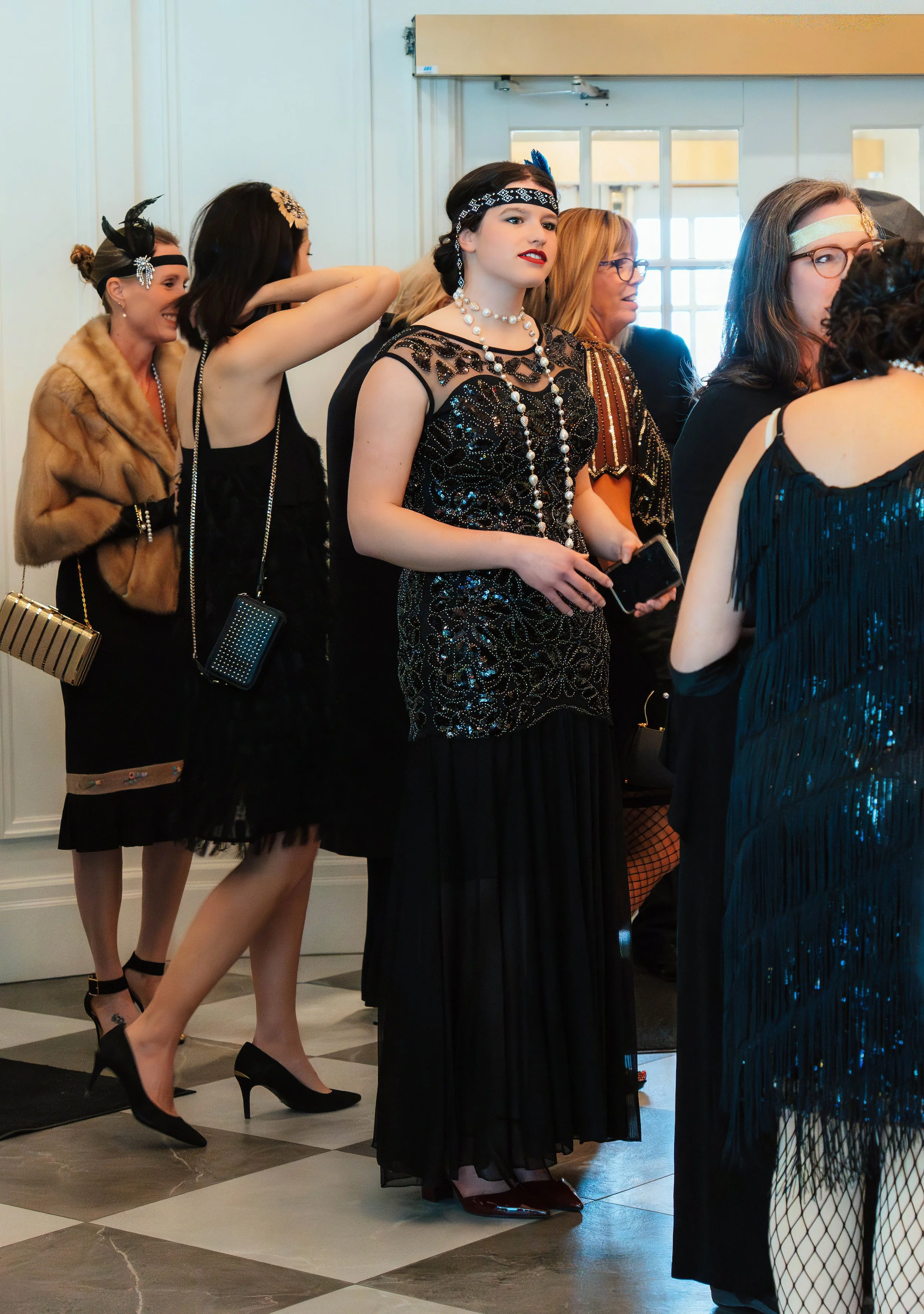 Women dressed in glamorous vintage 1920s-style attire at an indoor event.