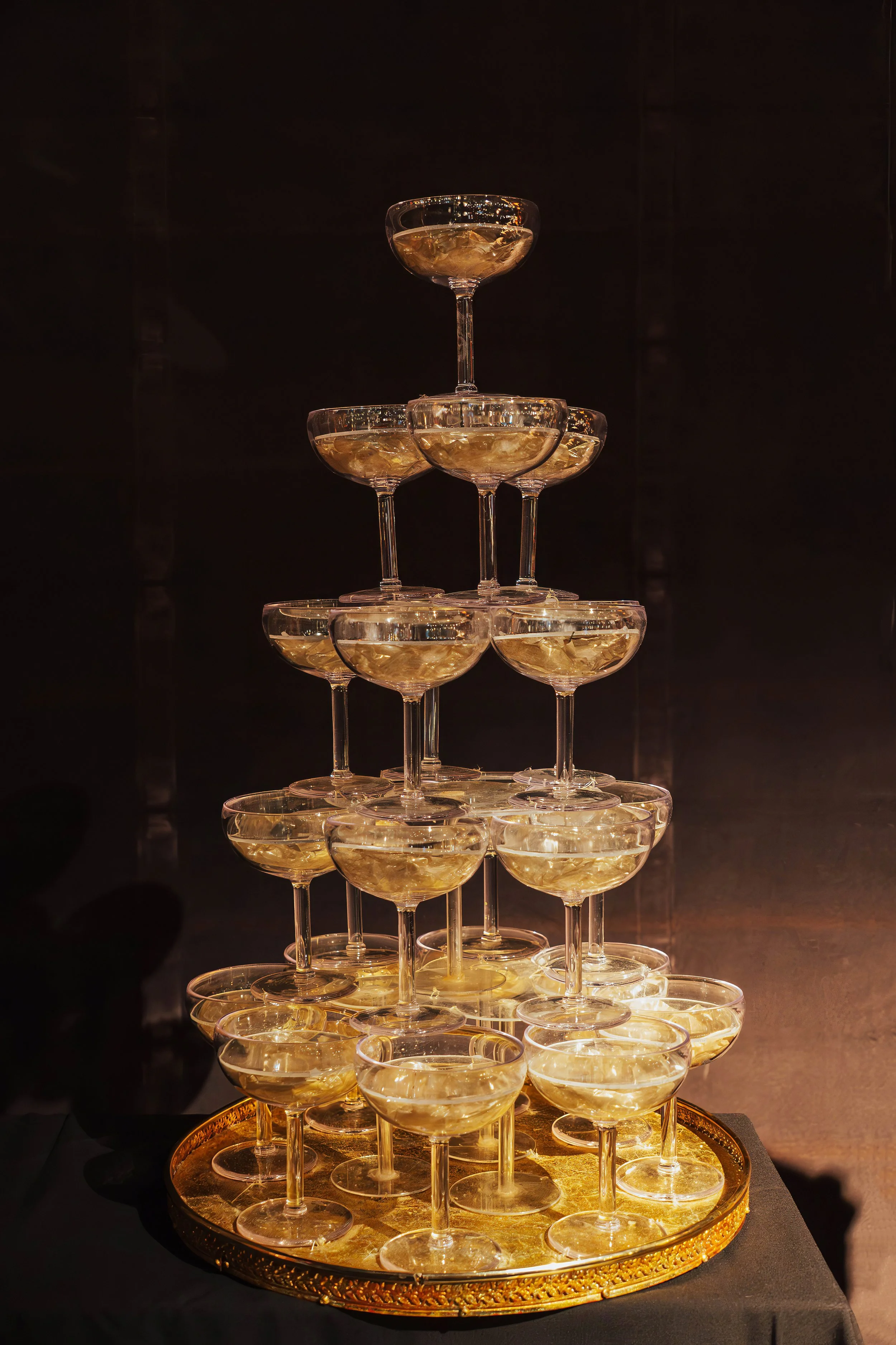 A pyramid of champagne glasses filled with champagne on a gold tray.