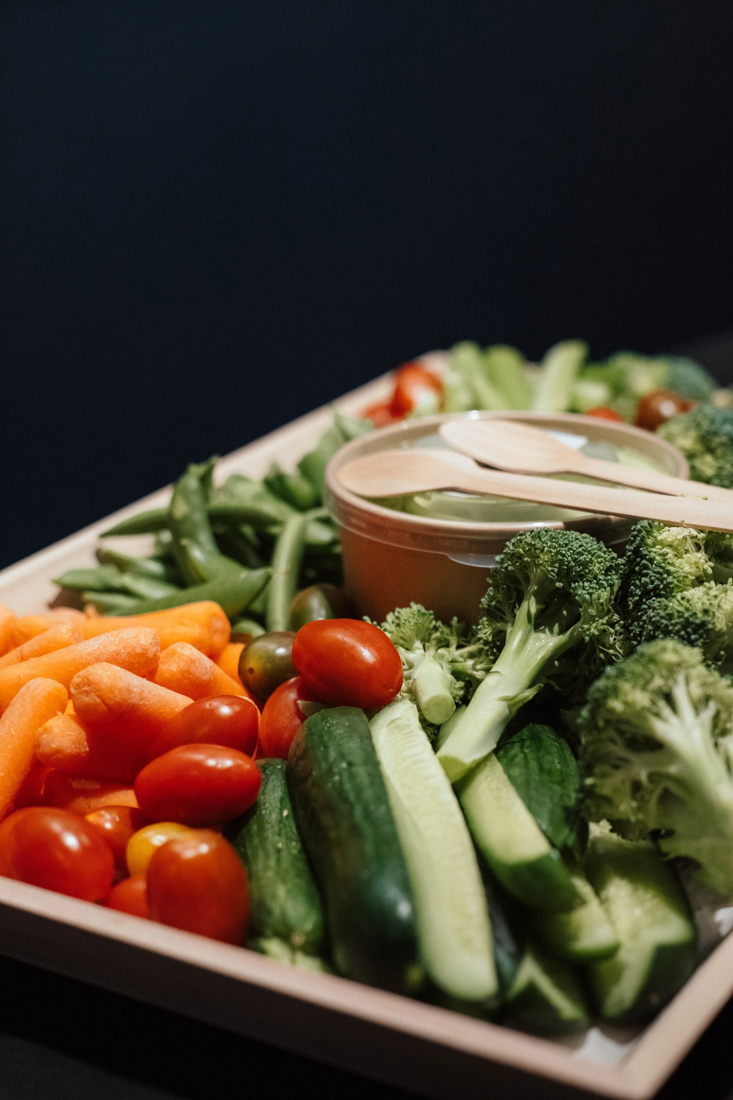 Fresh cut vegetables including cherry tomatoes, mini cucumbers, carrots, broccoli, and green beans on a tray with a small container of dip.
