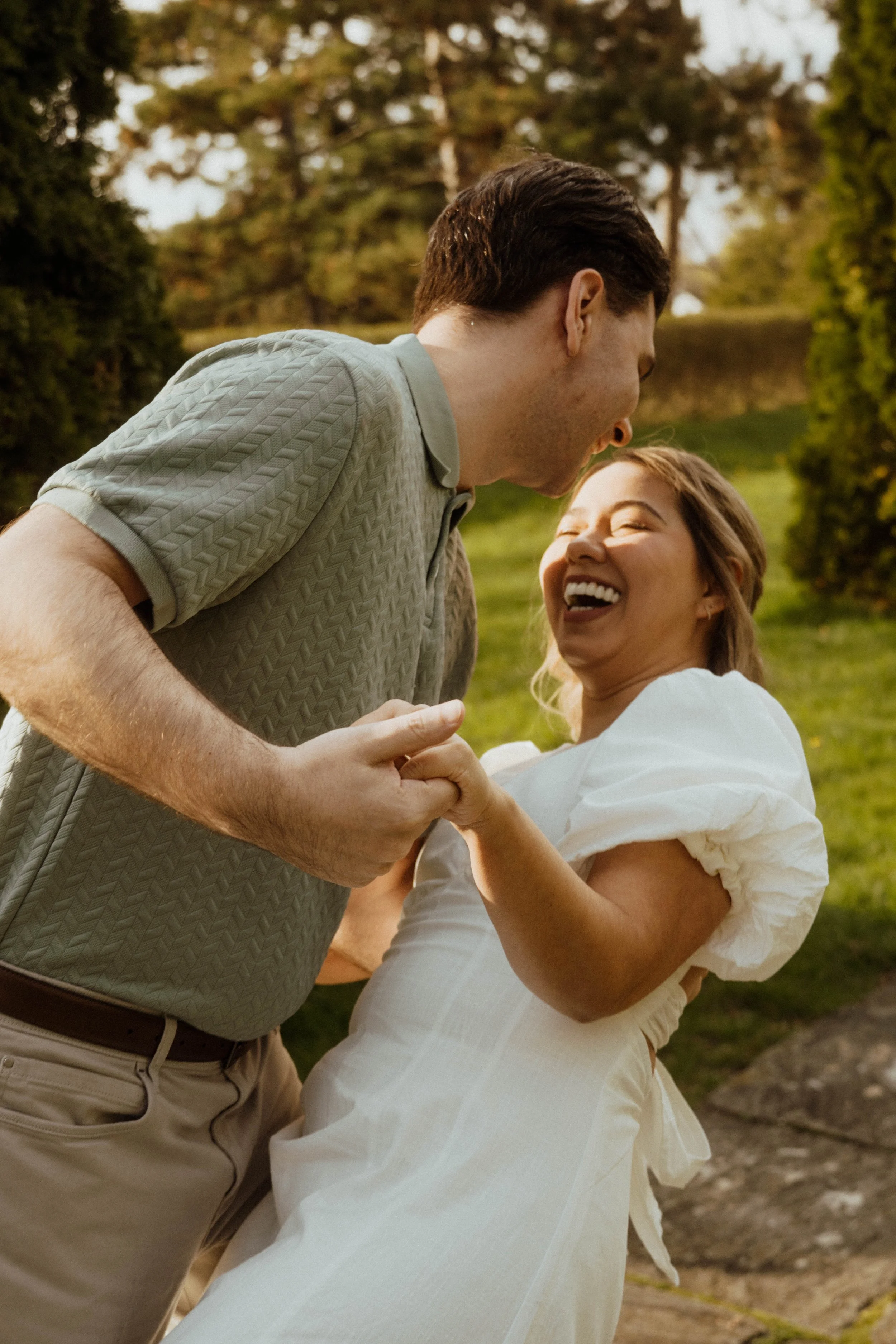 A couple sharing a joyful dance outdoors in a park with trees in the background.