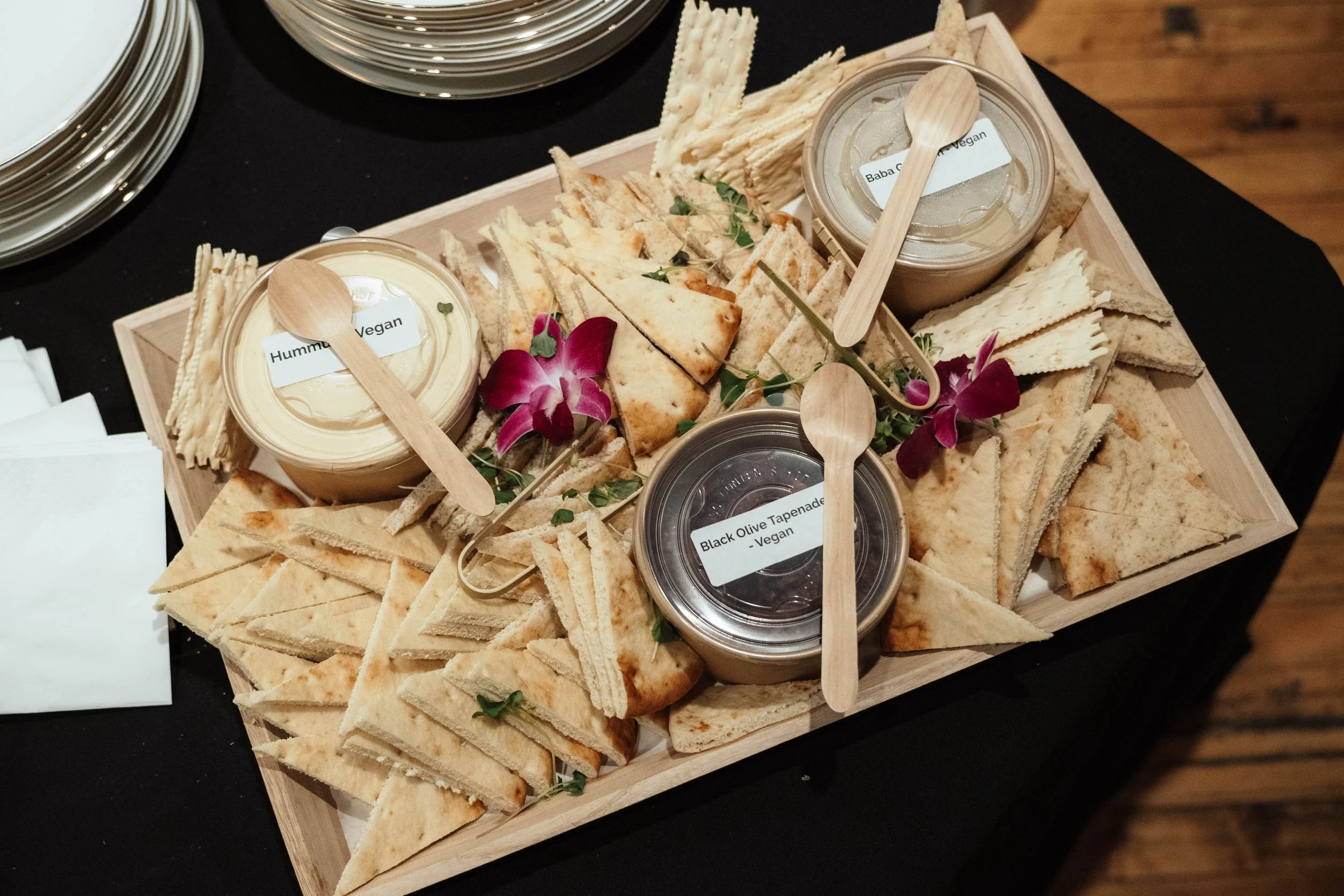 Tray of assorted vegan dips and pita chips, decorated with orchids and greenery.
