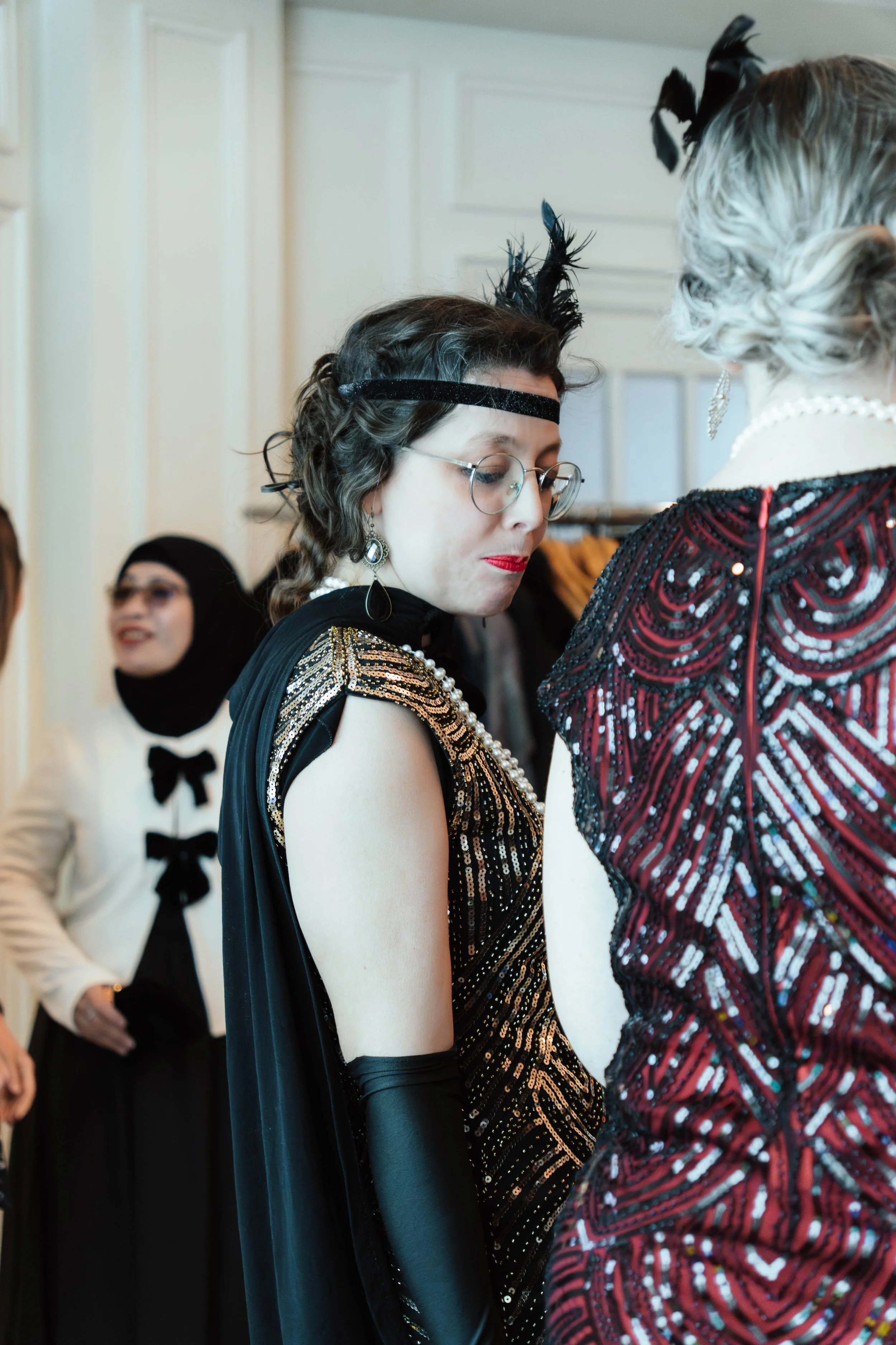 Women dressed in vintage flapper-style costumes with feather accessories, pearls, and glamorous makeup at a themed costume party.