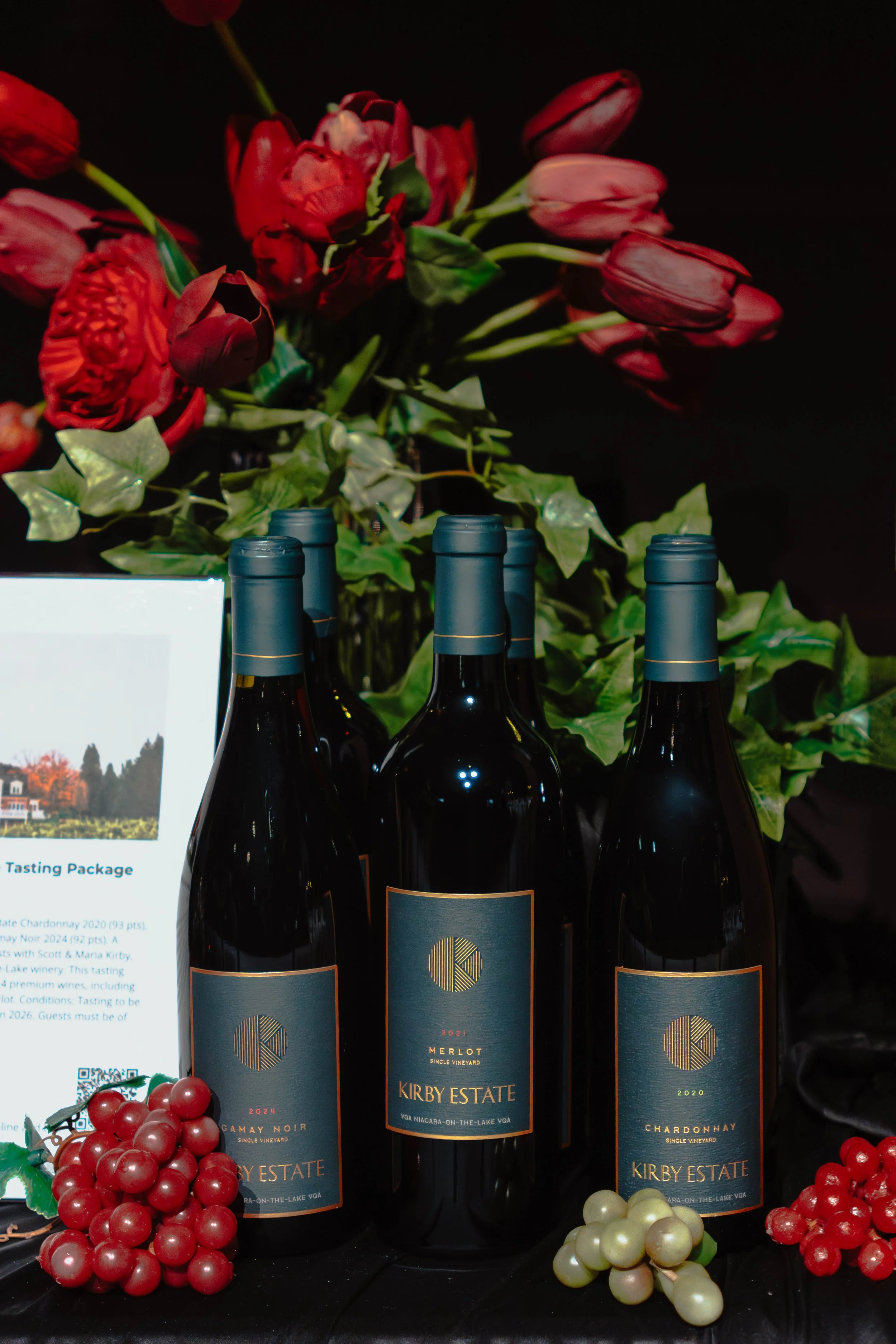 Three bottles of Kirby Estate wine, with grapes and flowers in the background.