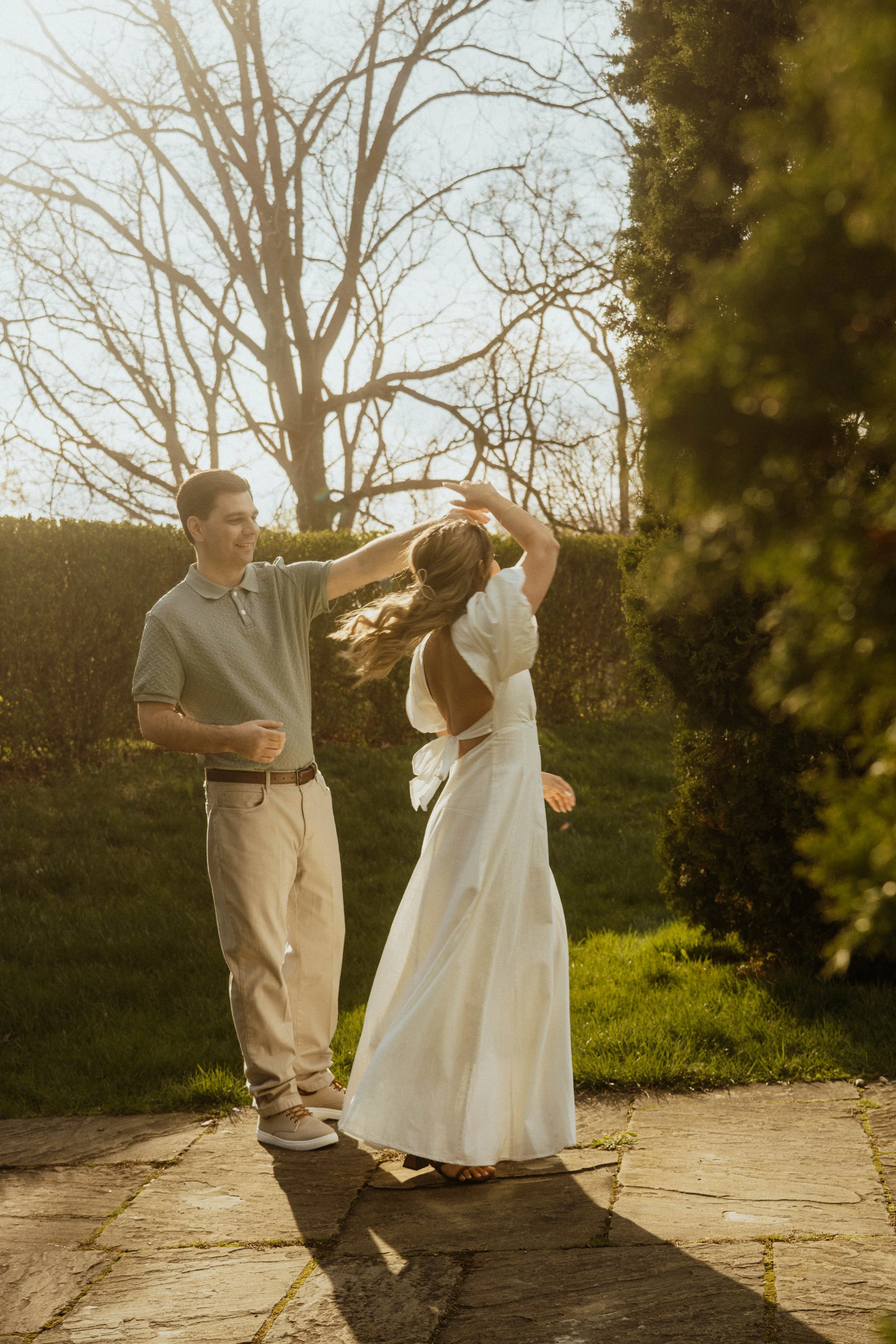 A man and woman dancing outdoors on a sunny day, with trees and bushes in the background.