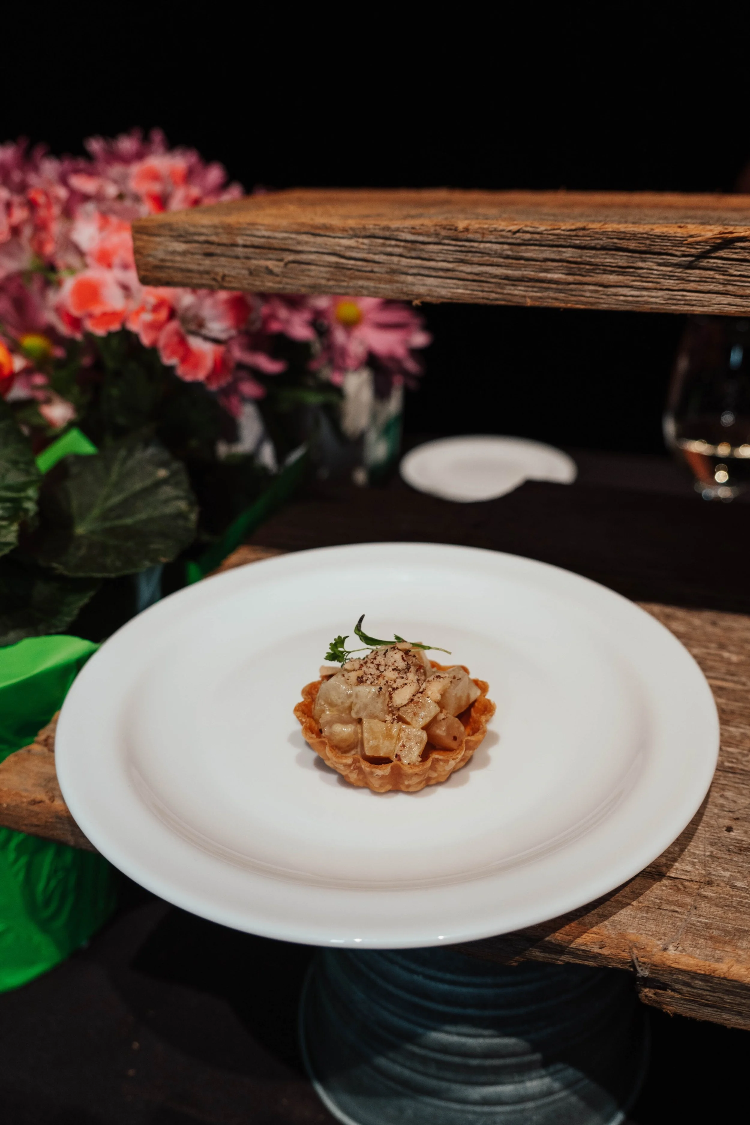 A small tart with diced apples, garnished with a sprig of herbs, on a white plate.