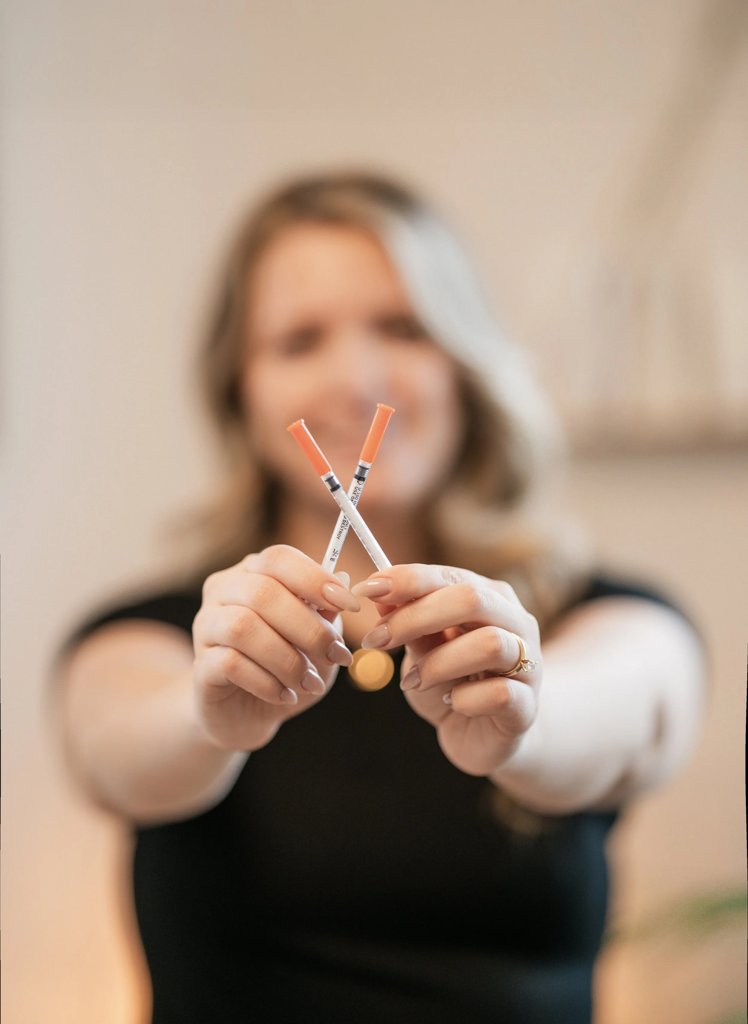 Beauty branding photo featuring a skincare injector holding syringes with soft luxury studio lighting and shallow depth of field.