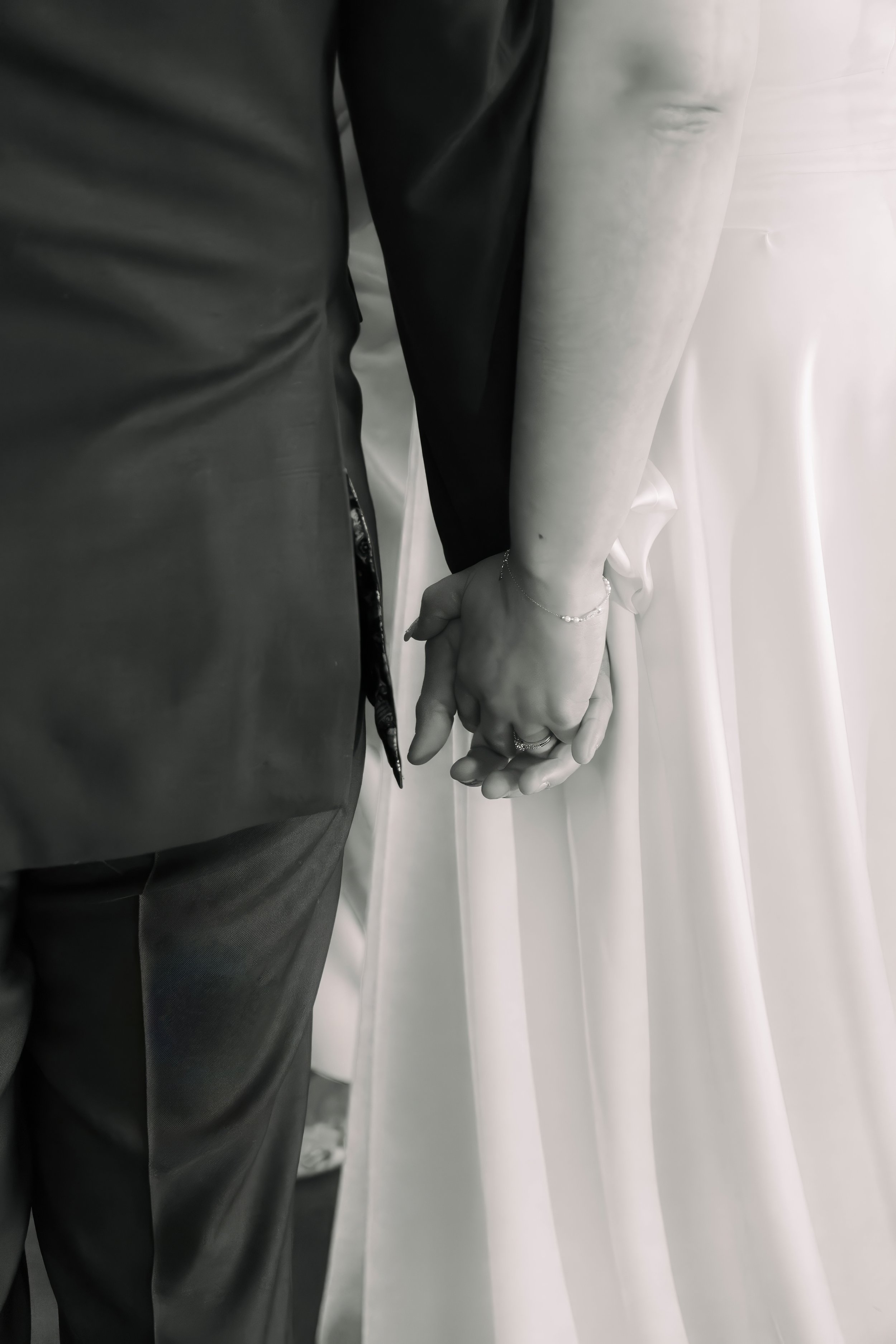 Close-up of a couple holding hands, with the woman wearing a wedding dress and the man in a suit, symbolizing marriage.
