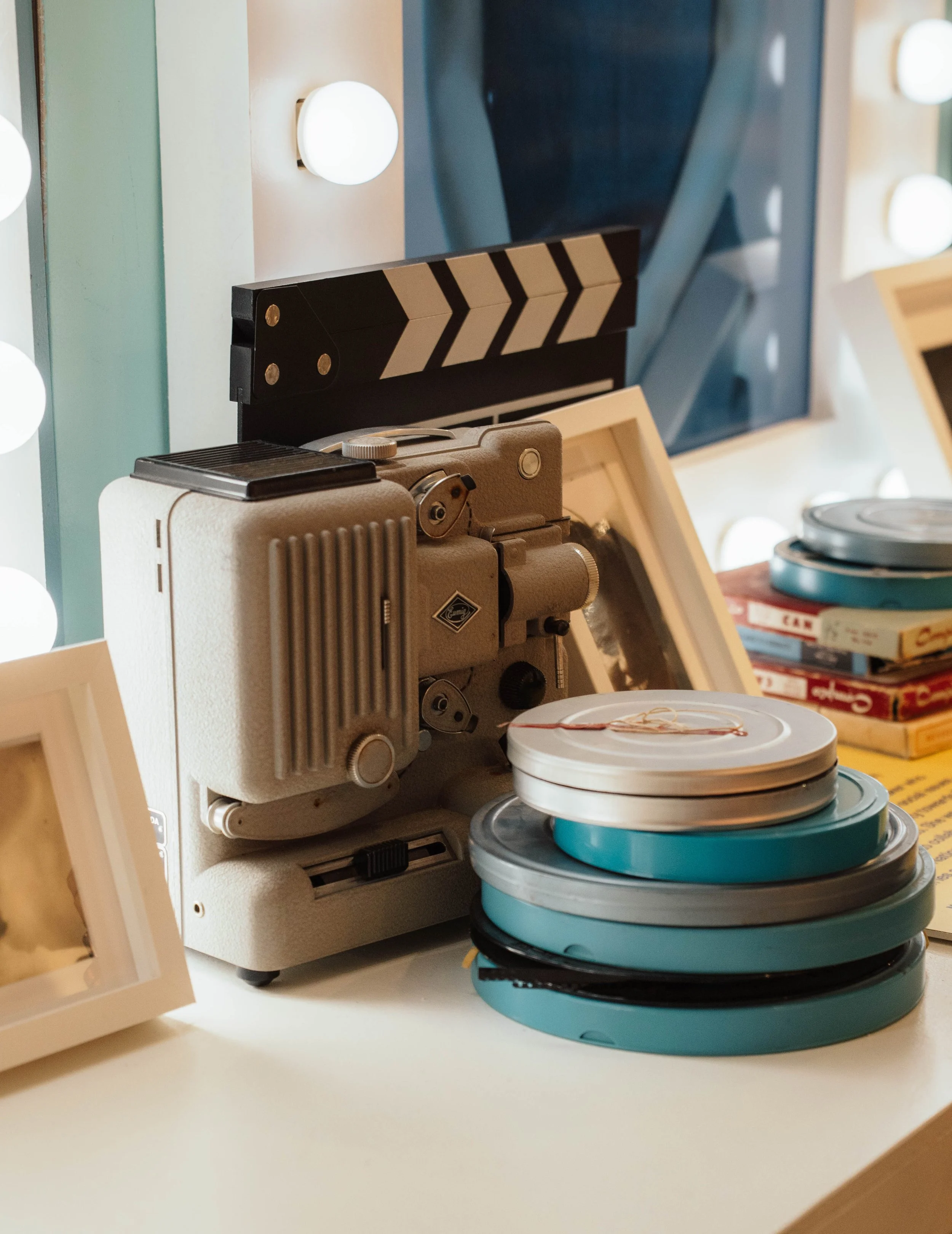 Vintage movie projector with film reels on a table, surrounded by framed photos and books.