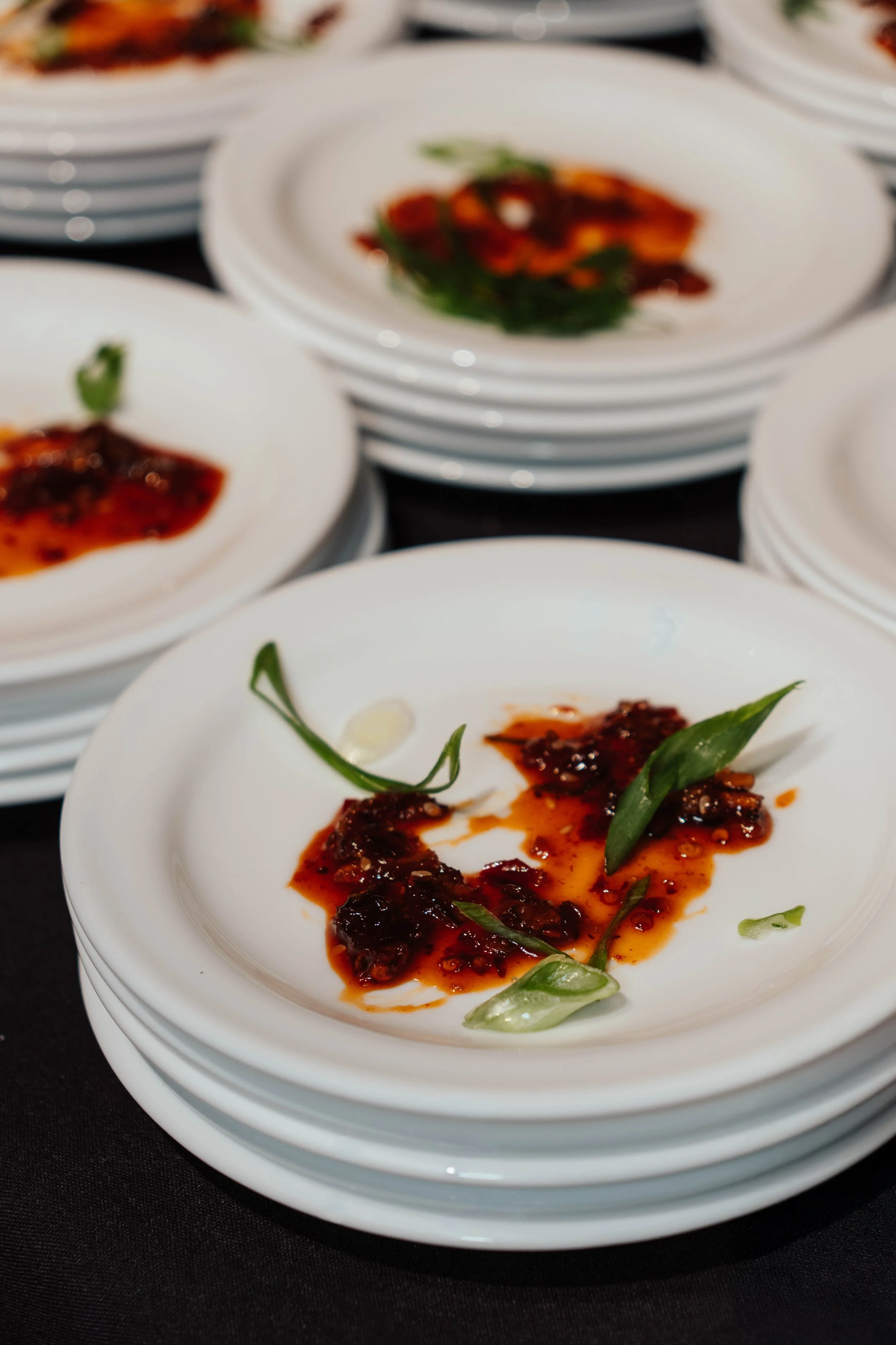 Stack of white plates with remaining fried crab with sauce and garnished with green herbs, on black table.