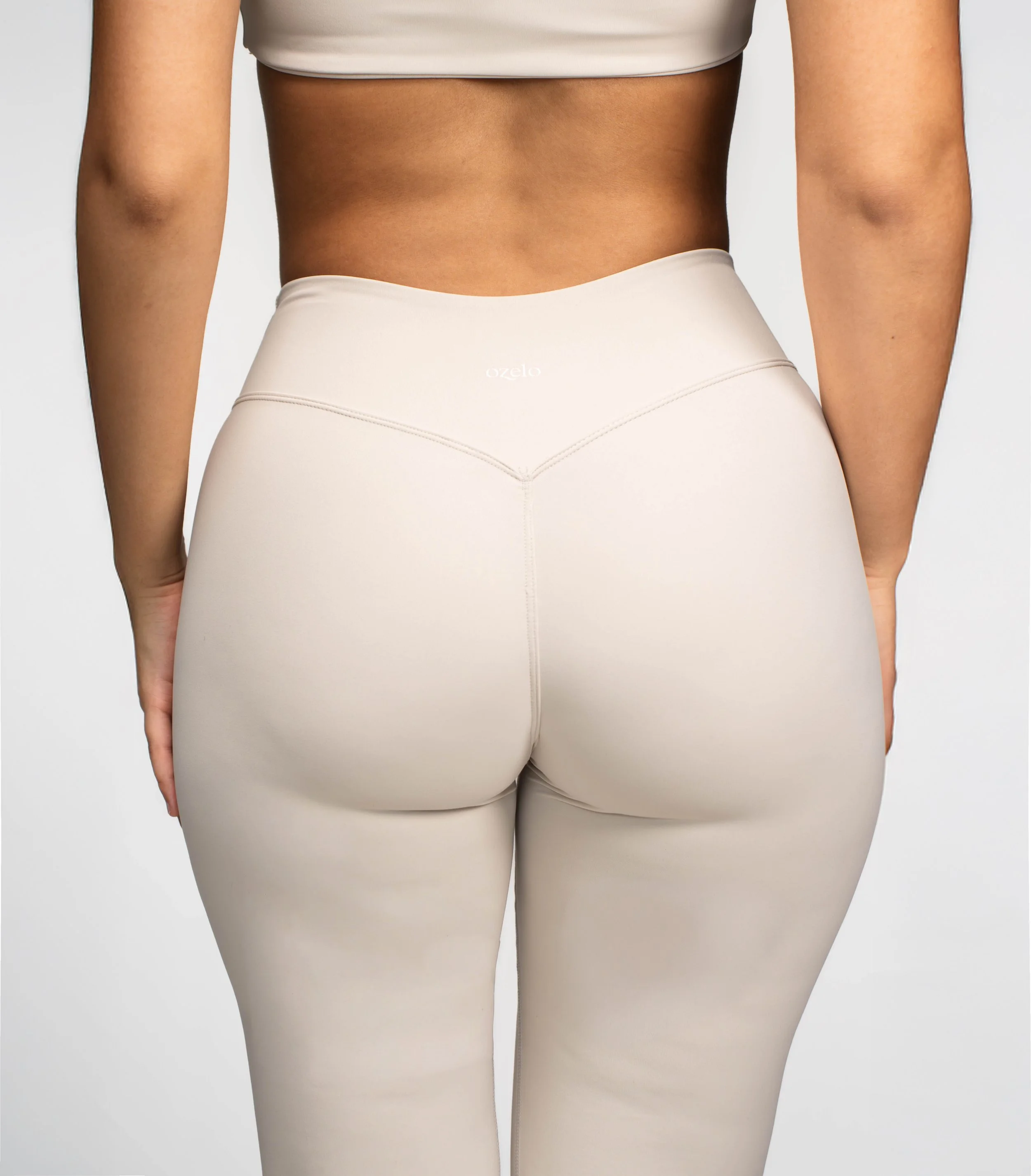 Back view of a woman wearing beige high-waisted leggings and a white crop top.