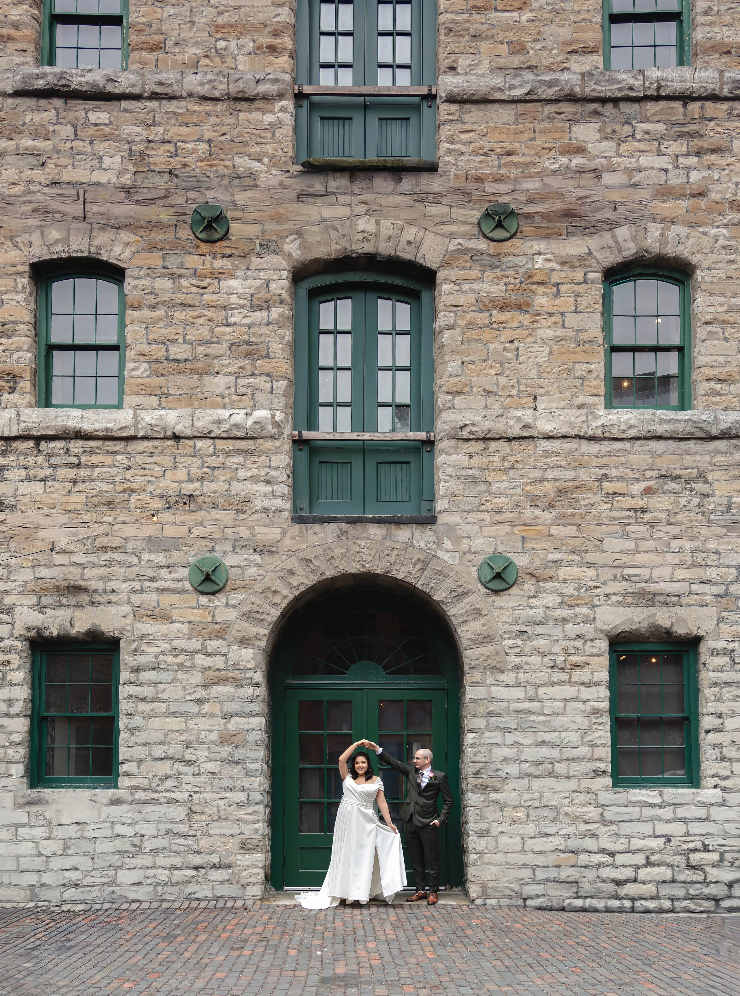 Bride and groom posing in front of historic stone architecture at Toronto’s Distillery District during an intimate cinematic wedding photoshoot.