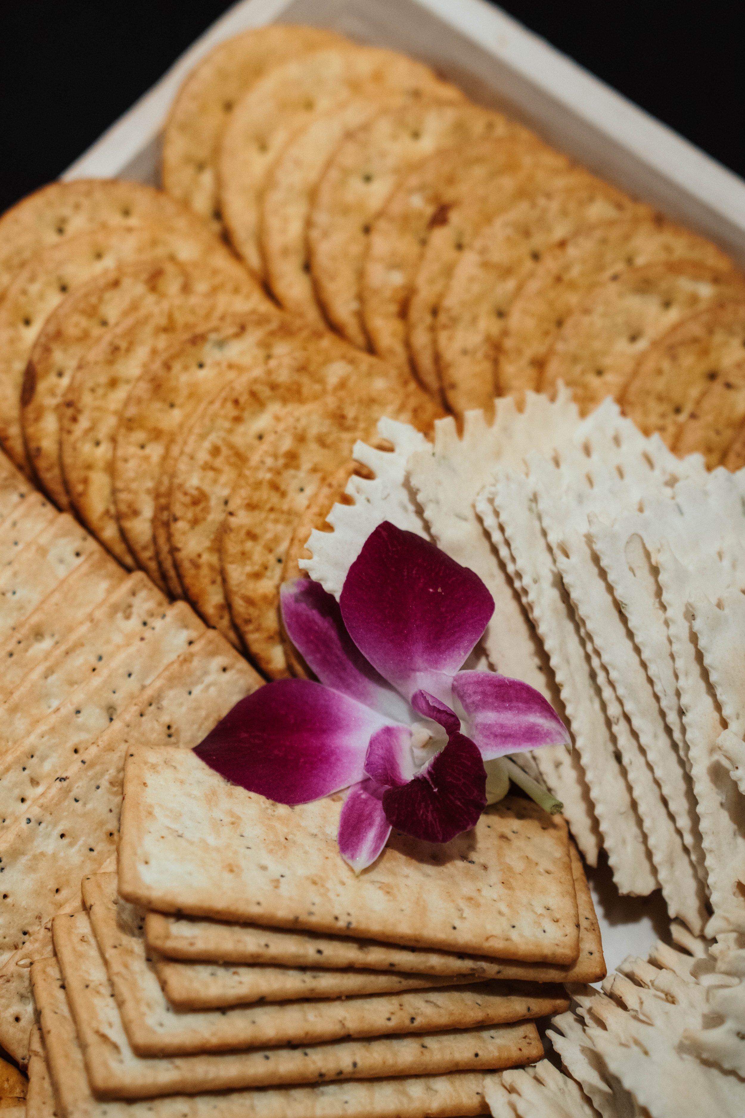 Assorted crackers arranged on a tray with a purple orchid flower for decoration.