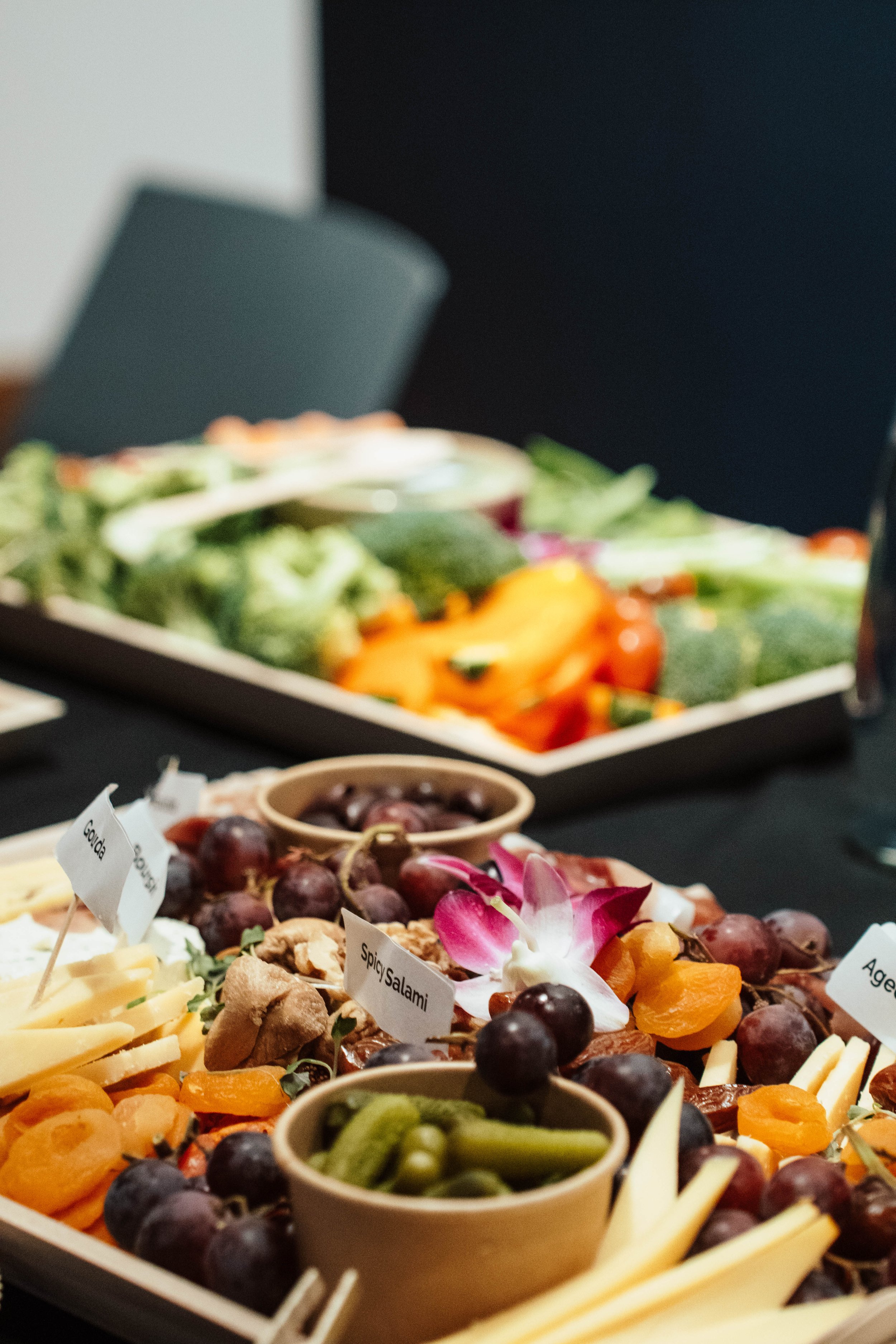 Tray of assorted cheeses, grapes, and vegetables on a table at a buffet or party.