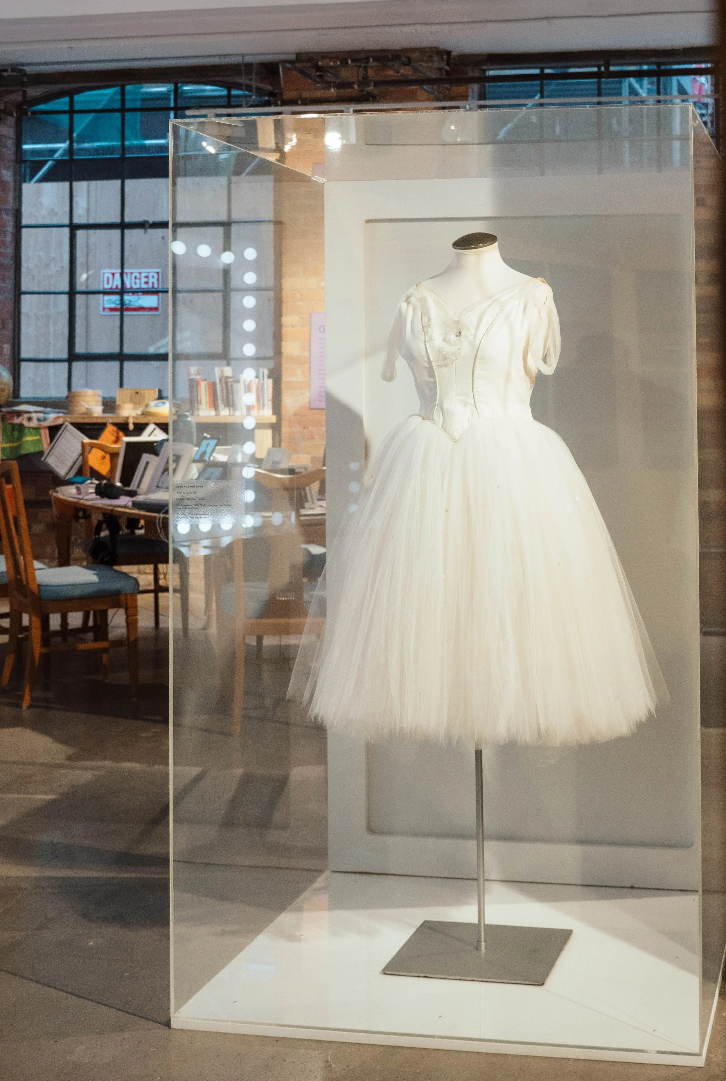 A vintage white wedding dress on a mannequin inside a glass display case in a modern industrial-style space.