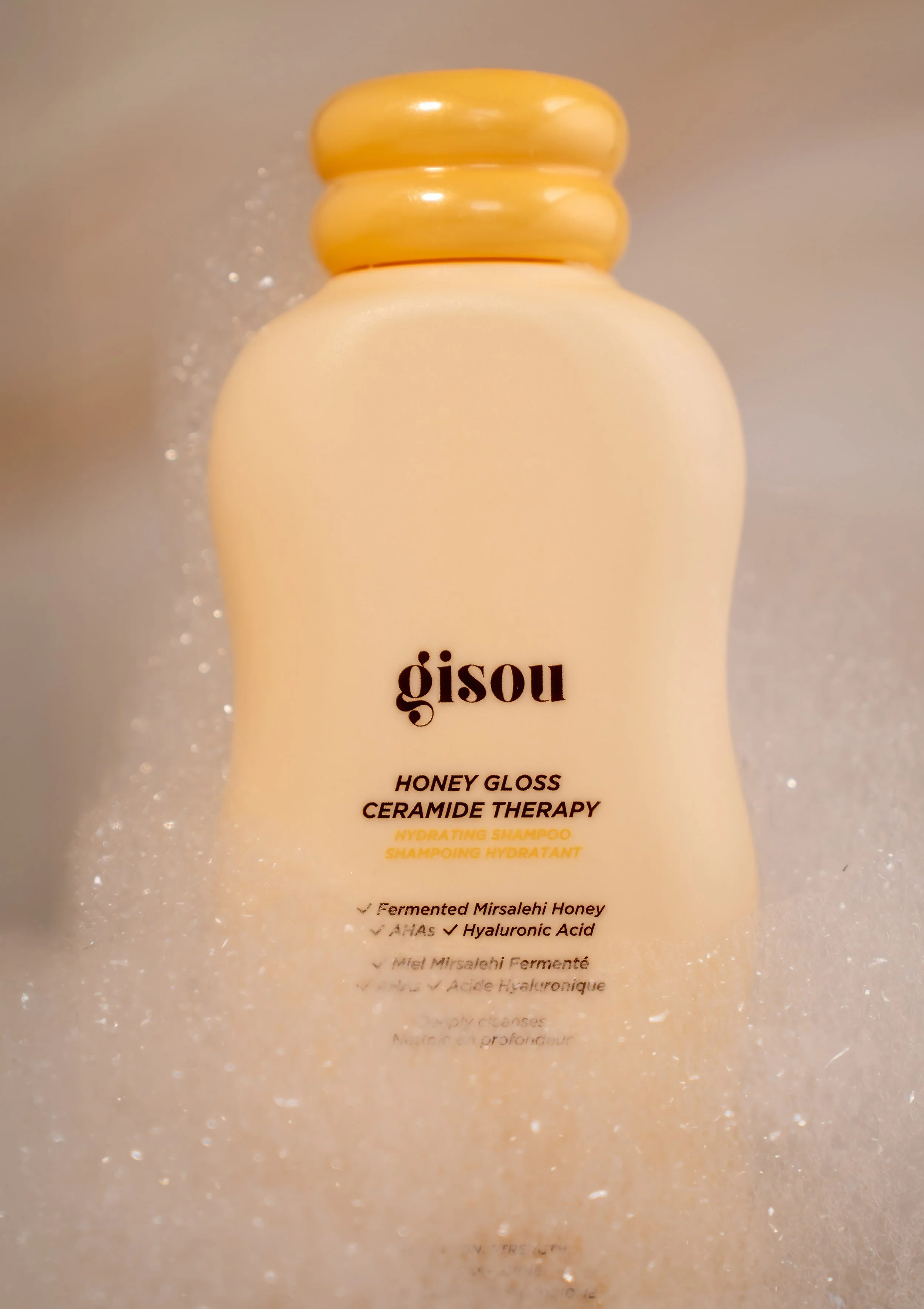 Bottle of Gisou Honey Gloss Ceramide Therapy hydrating shampoo with water droplets on it.