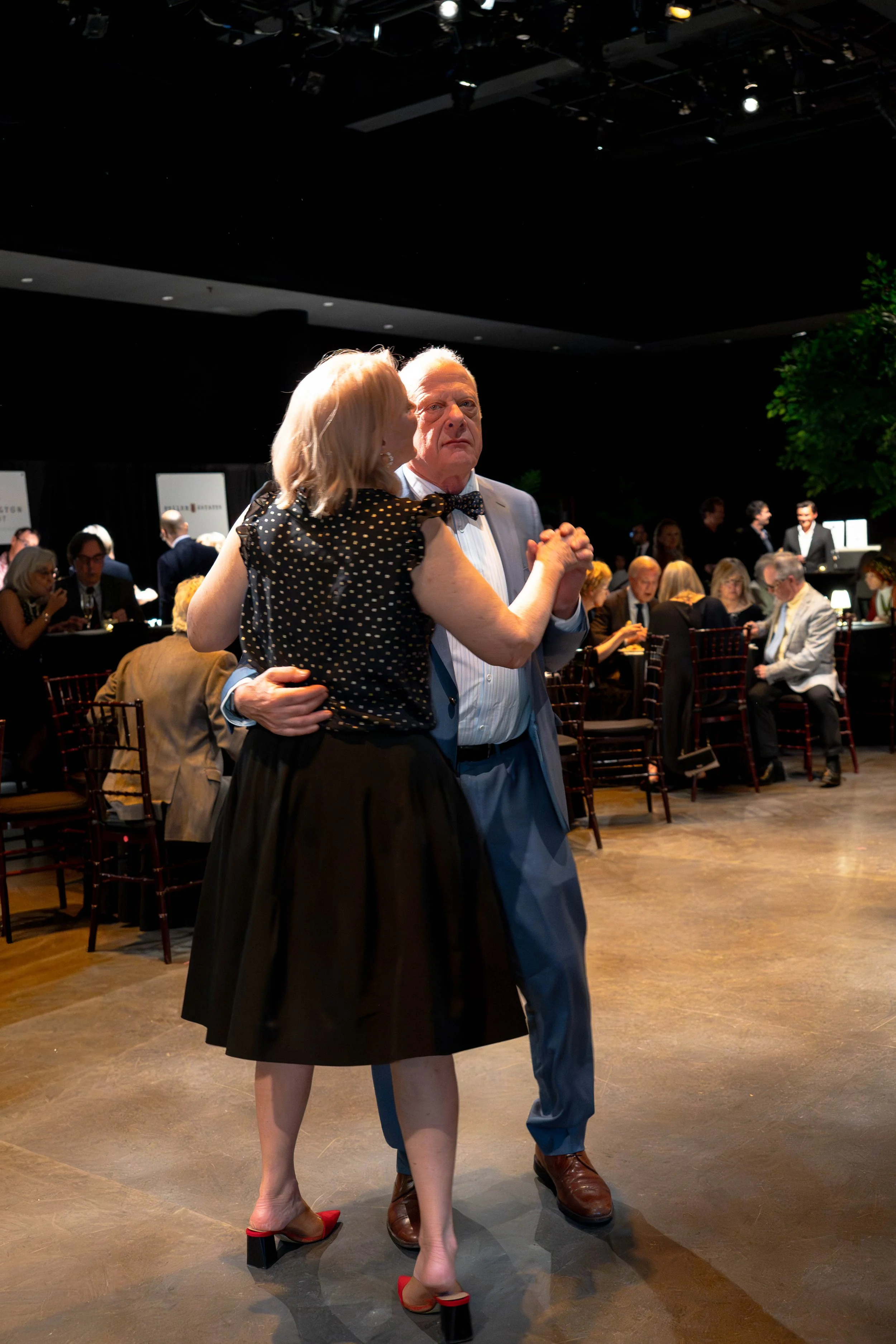A couple dancing at a formal event with seated guests in the background.