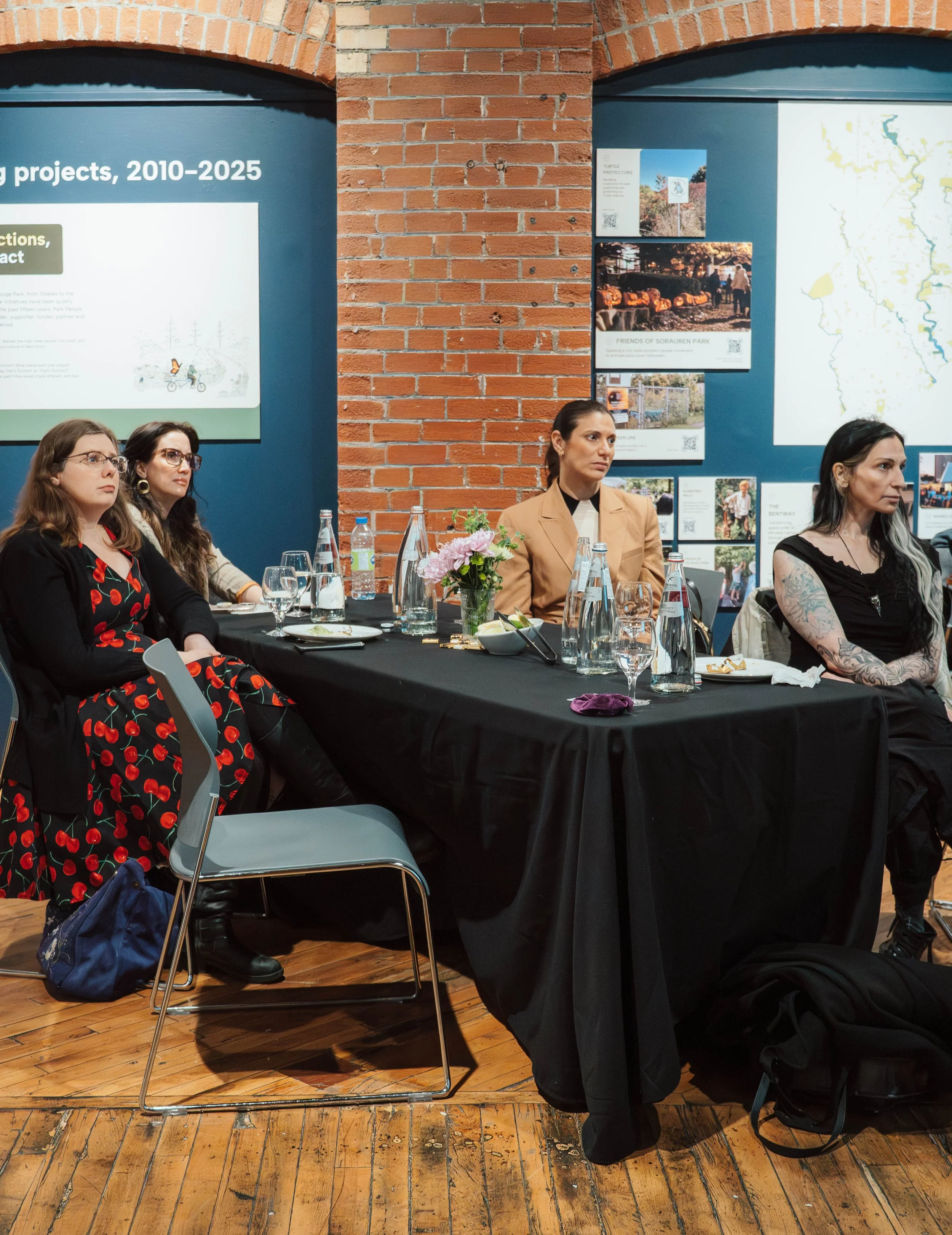 Four women sitting at a conference table during a meeting, with informational posters and a map on the blue wall behind them.