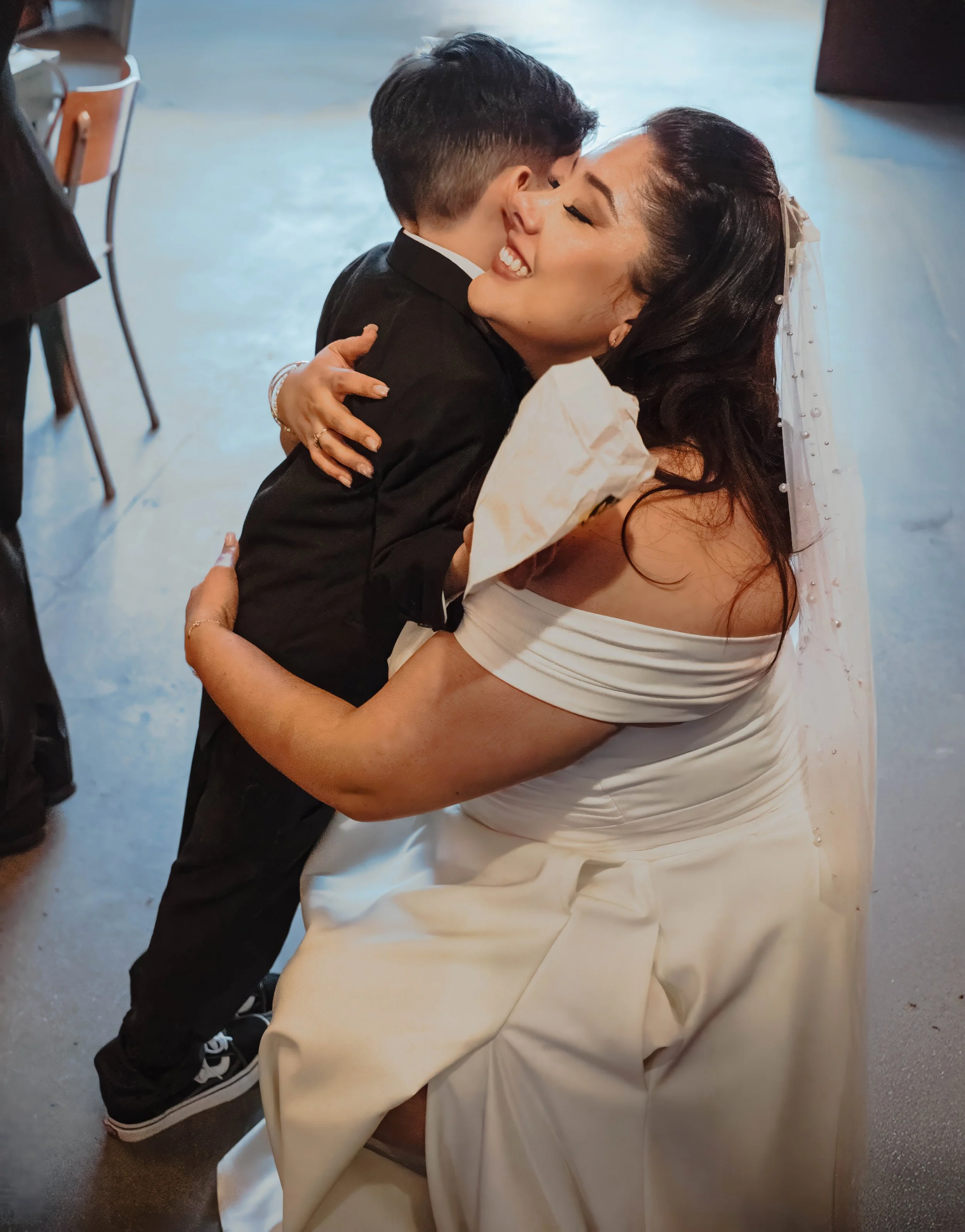 A woman in a wedding dress hugging a young boy in a tuxedo at a wedding reception.