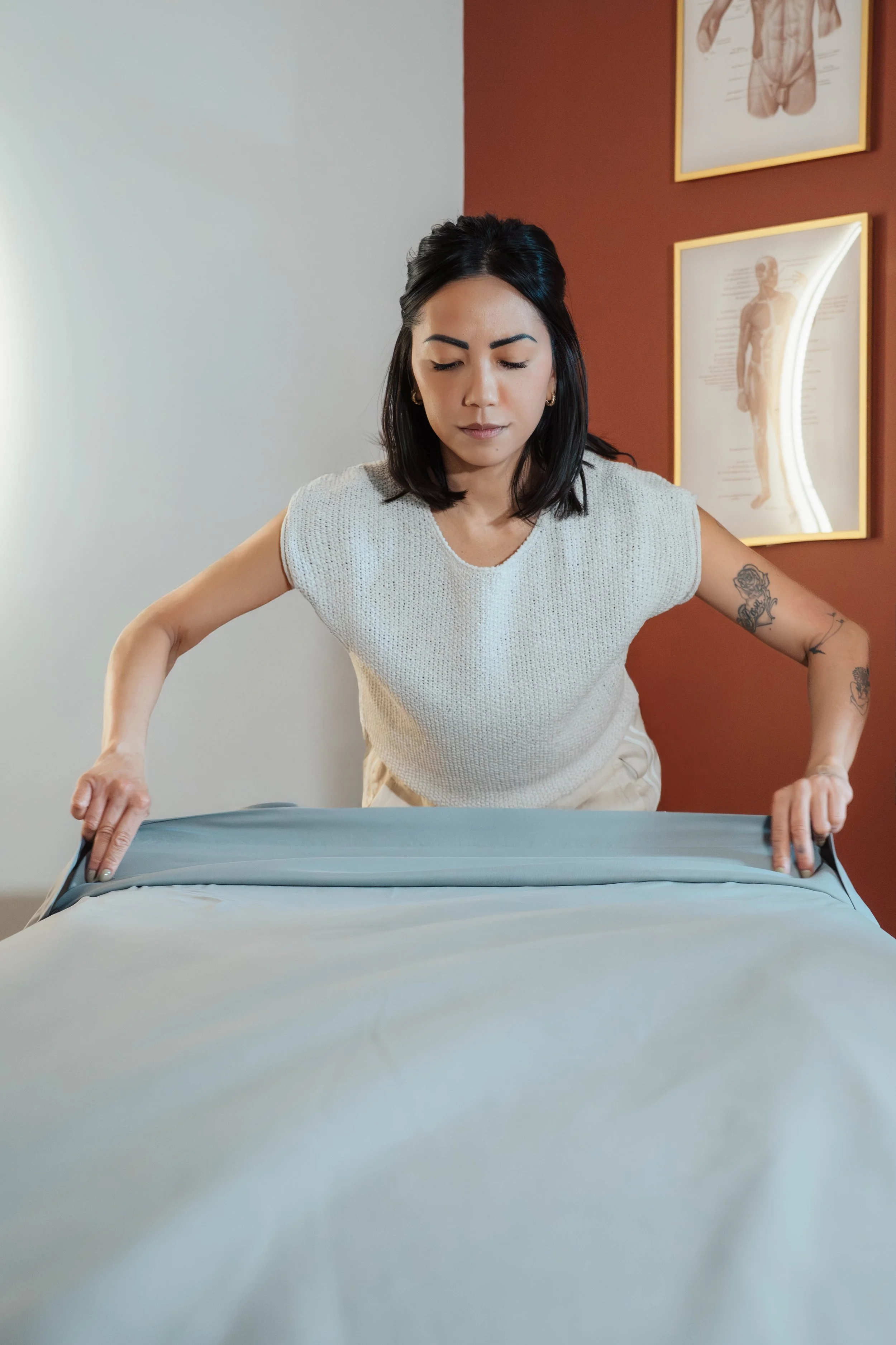 Woman making a bed in a room with anatomical posters on the wall.