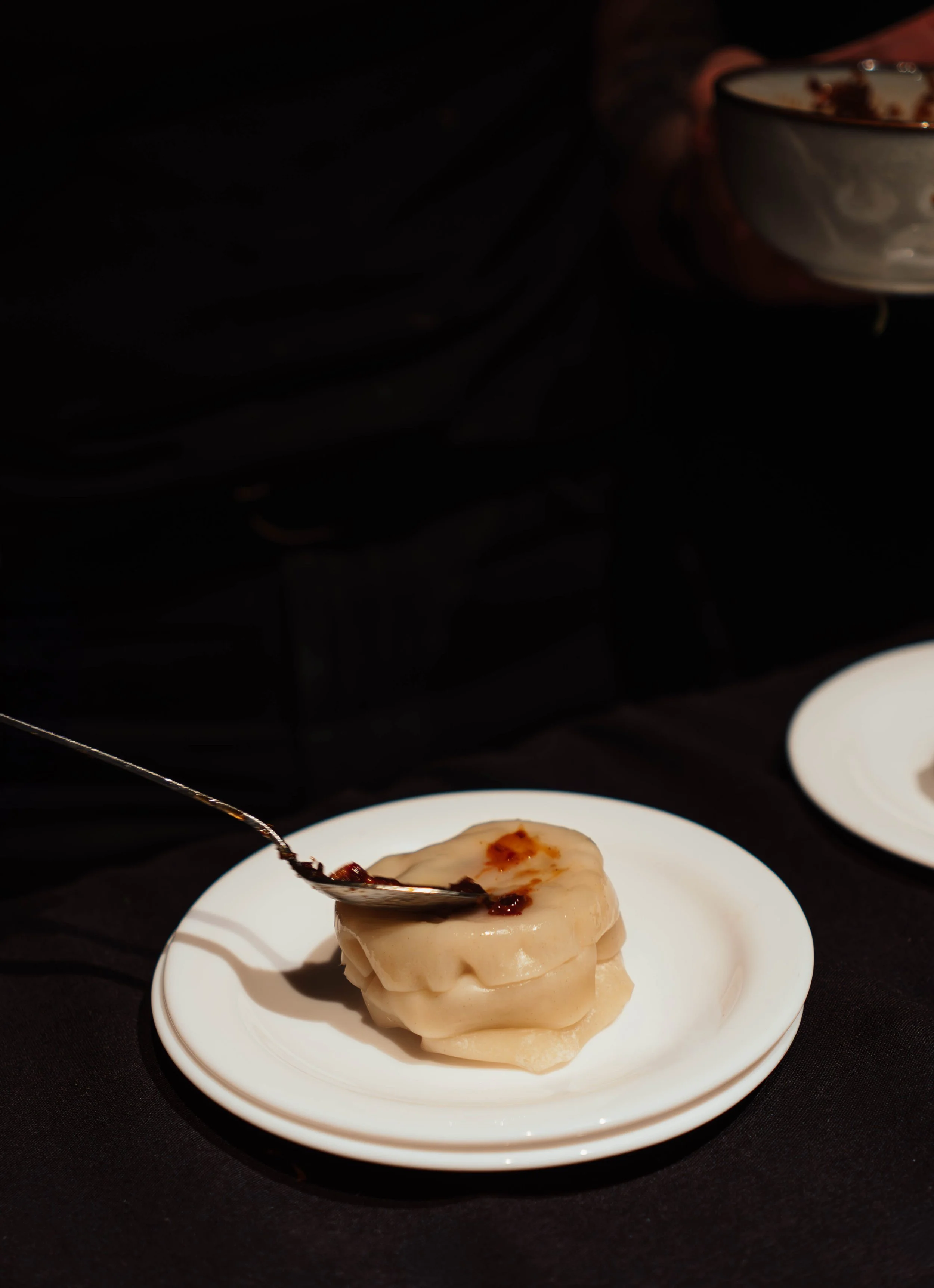A stack of three dumplings on a white plate with some dark sauce on top, with a spoon resting on the dumplings.